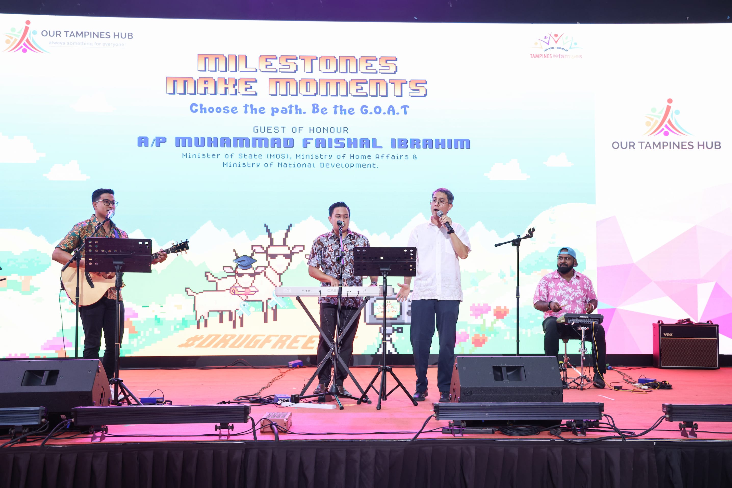 Three musicians perform on stage with "Our Tampines Hub" logo, and a backdrop of event details.