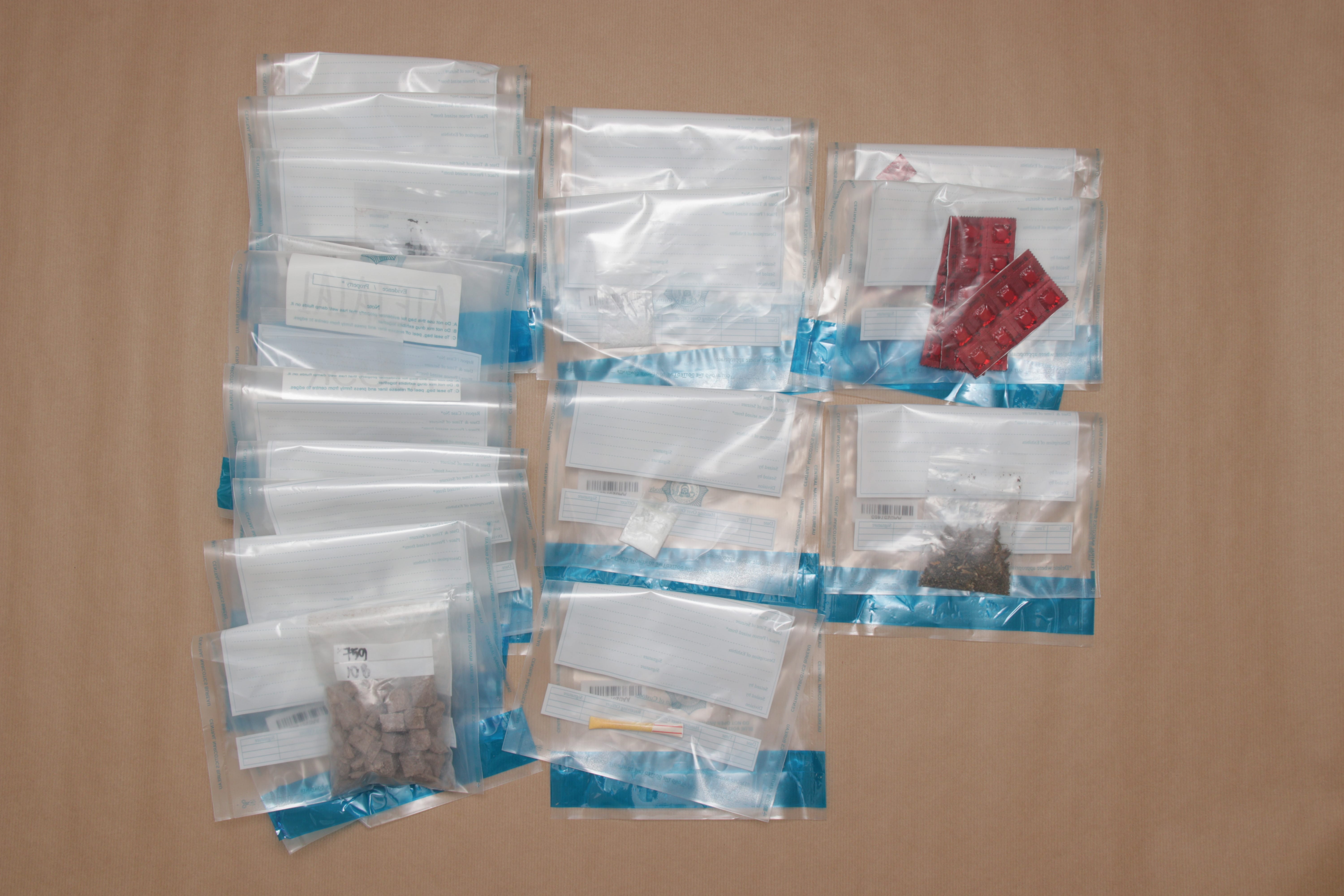 Evidence bags: pills, brown chunks, white powder, and plant matter on a brown surface.