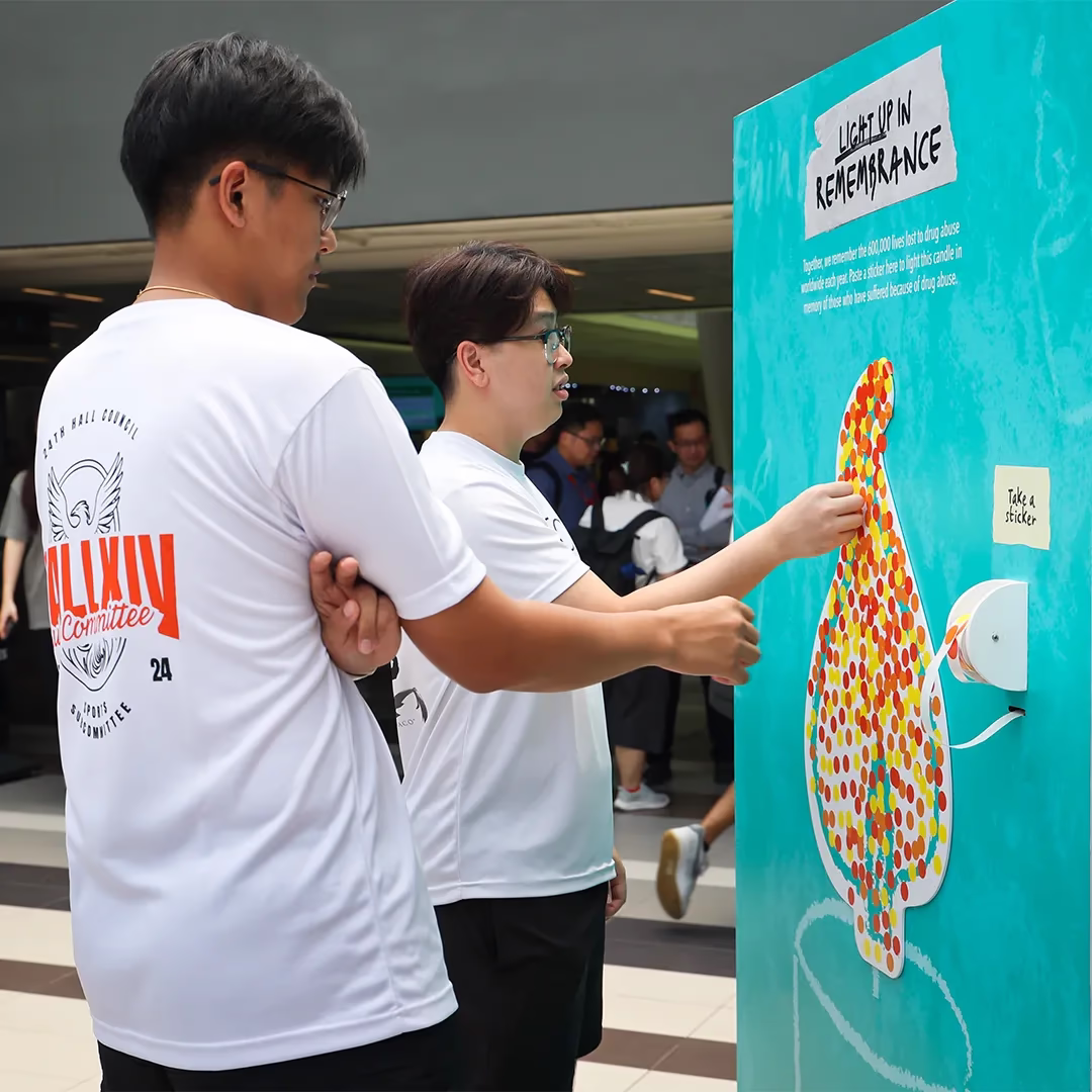 Two participants place stickers on a flame-shaped board for the “Light Up in Remembrance” activity.