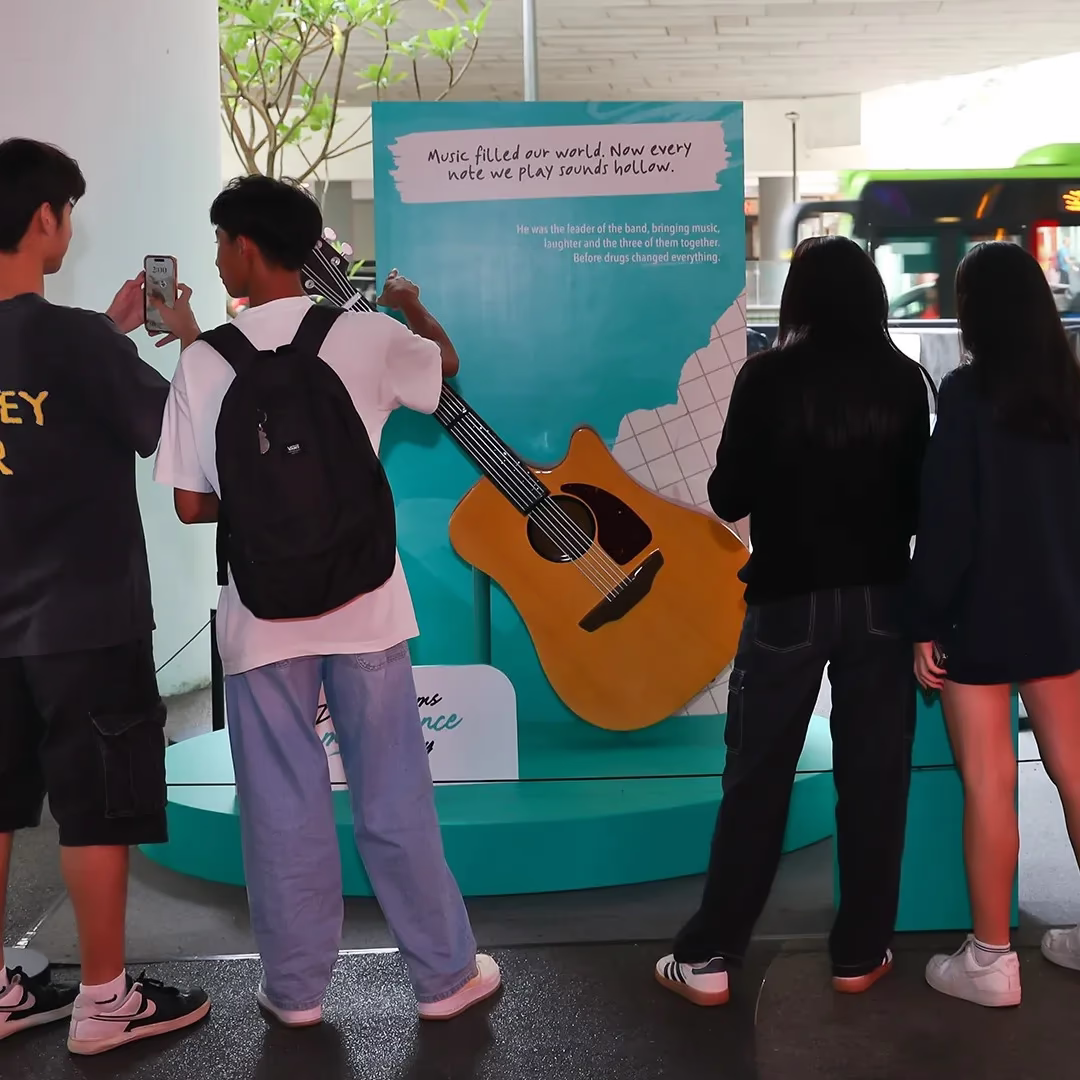 Four people, seen from behind, looking at a large guitar display with a Drug Victims Remembrance Day sign.