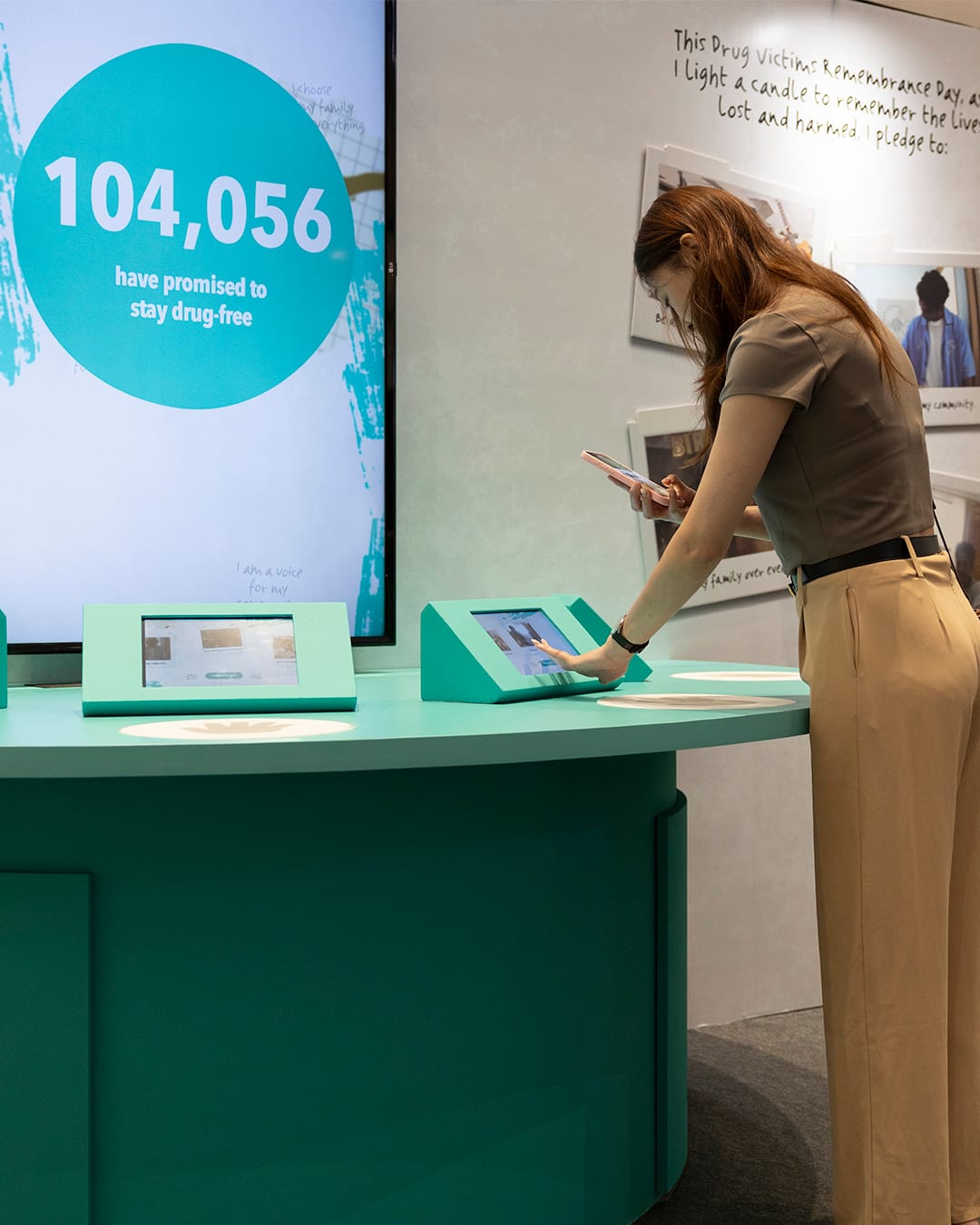 Visitor using teal touchscreen; nearby display reads “104,056 have promised to stay drug-free.”