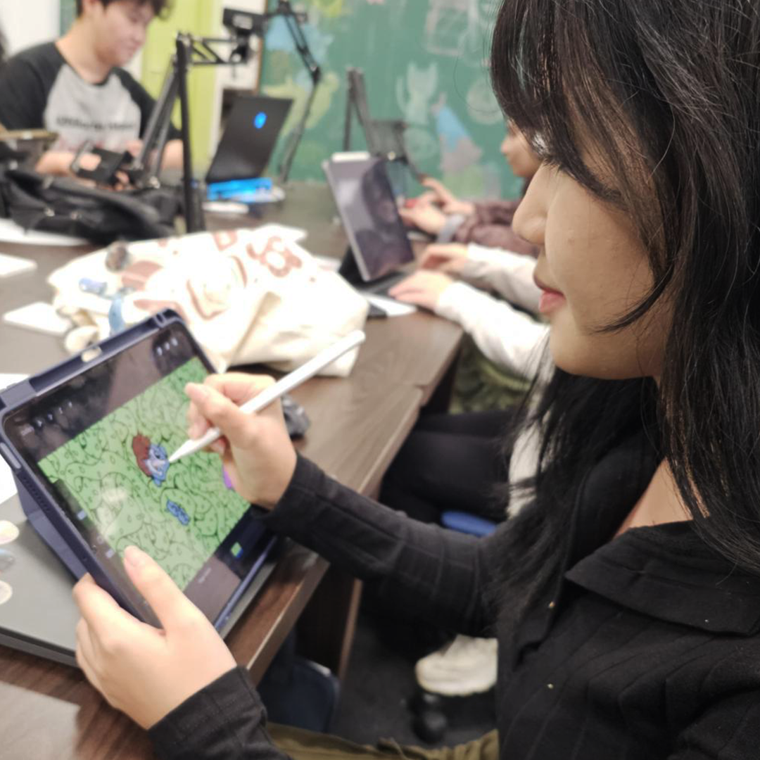 Young woman draws a character on a tablet during a group digital art session.