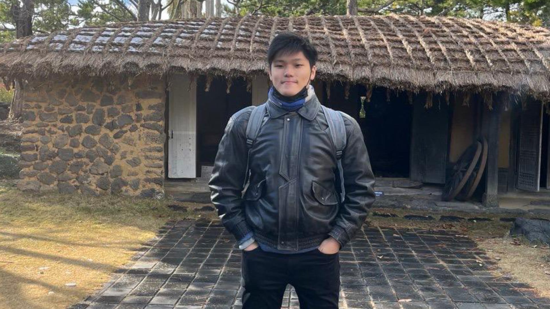 A student standing outdoors in front of a rustic building, wearing a jacket and backpack, representing a Built Environment scholar on a learning journey.