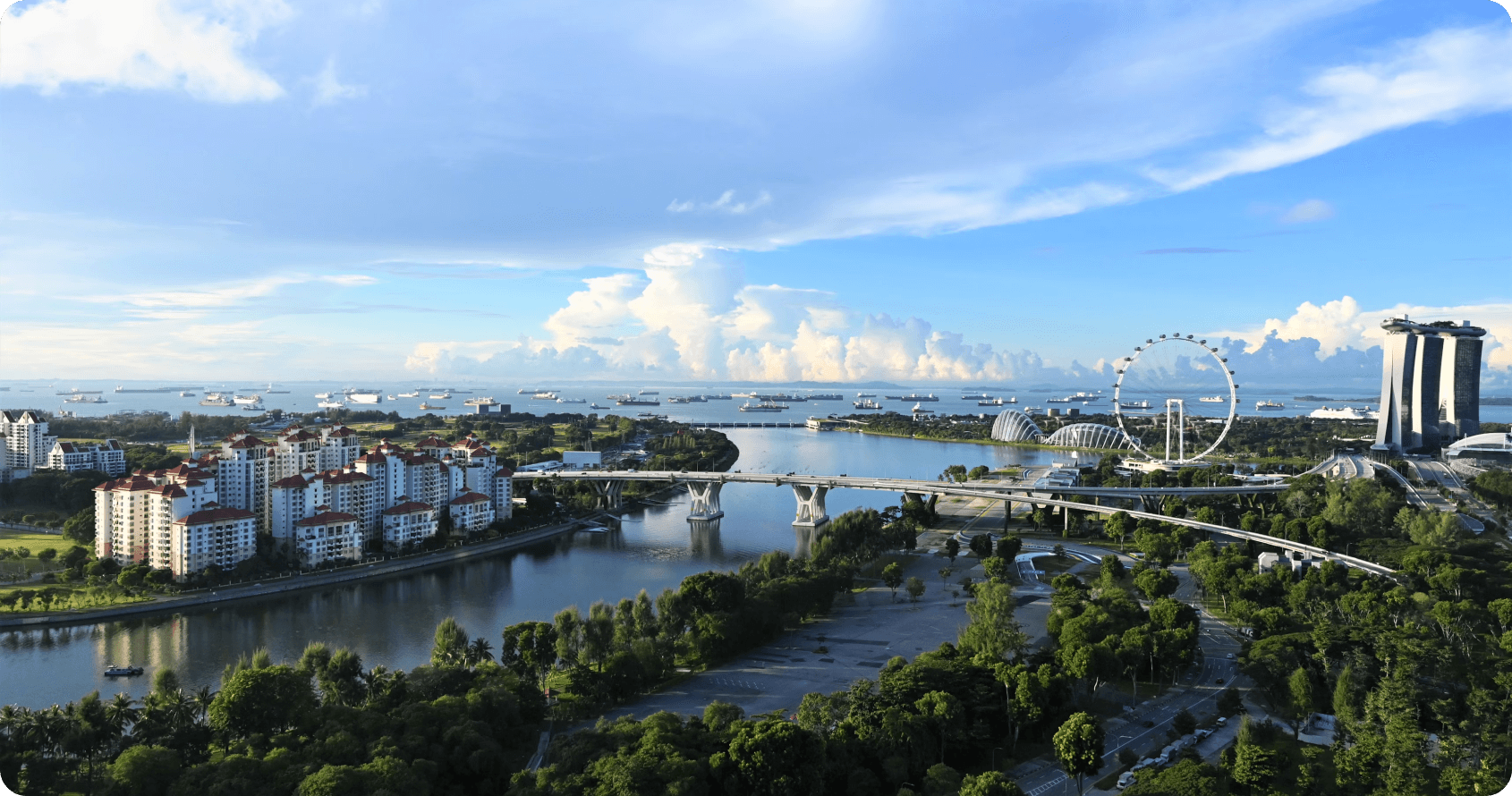 Singapore's Marina Bay development showcasing major built environment achievements including the iconic Marina Bay Sands integrated resort, Singapore Flyer observation wheel, and active maritime infrastructure. The waterfront demonstrates Singapore's urban planning excellence and construction capabilities under typical tropical sky conditions.
