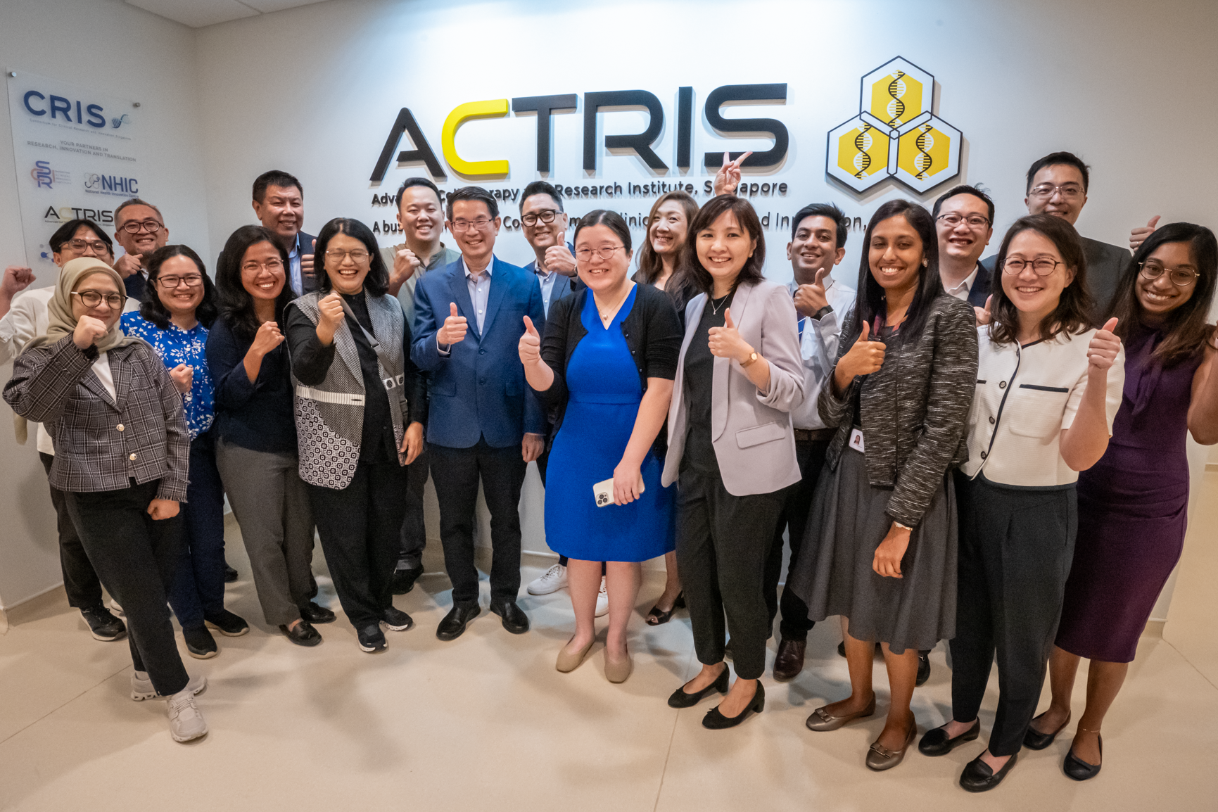 A group of people stands in front of a wall with the ACTRIS logo, holding thumbs up and various hand signs.
