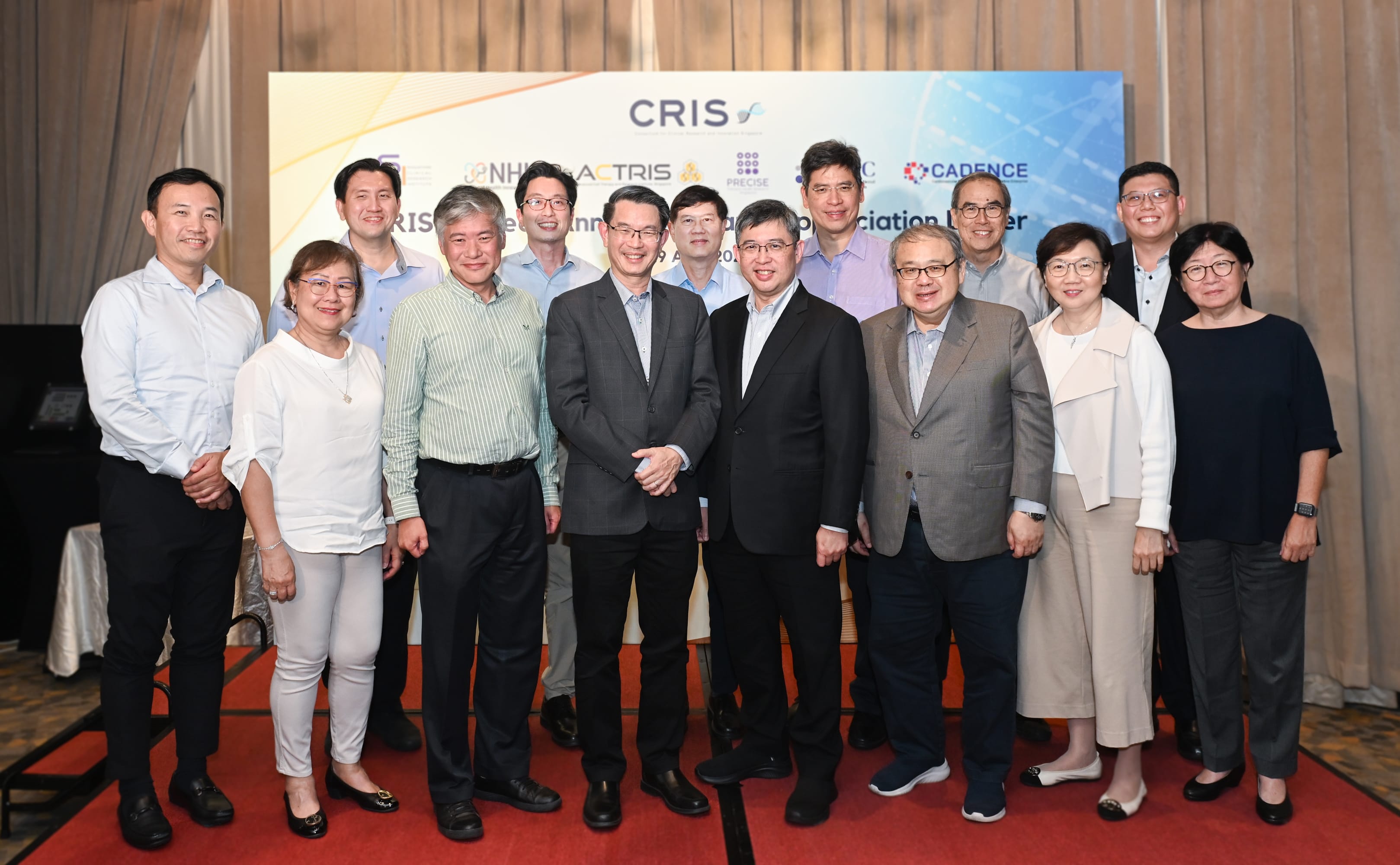 11 individuals stand on a red carpet in front of a banner with logos of CRIS, NH-ATRIS, PRECISE, IMEC, and Cadence.