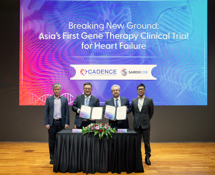 Four men in suits stand at a table with documents, flowers, and a sign that reads "Asia's First Gene Therapy Clinical Trial for Heart Failure."