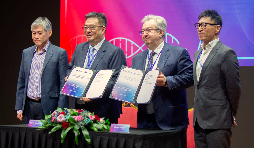 Four men in suits standing behind a table with certificates, flowers, and a name card.