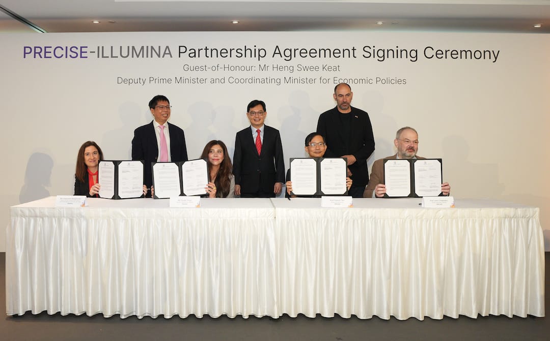 Six individuals stand and sit in front of a wall banner at a signing ceremony, holding up documents.