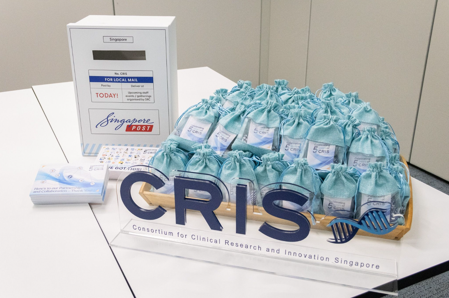 A display with a Singapore Post mailbox, CRIS banner, and numerous aqua-colored drawstring gift bags on a table.