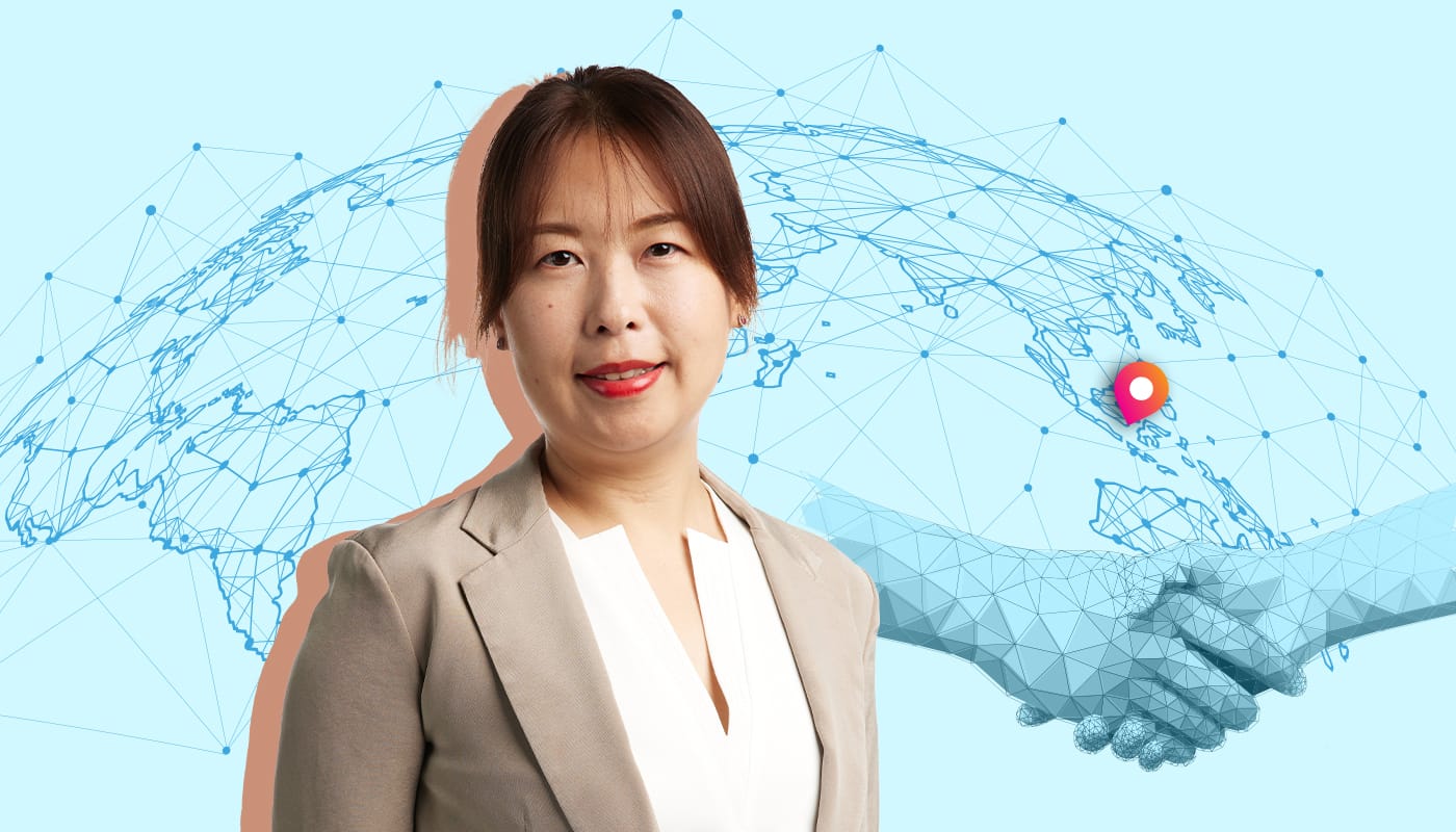 A woman in a blazer stands in front of a digital world map with a red location pin and handshake graphic.