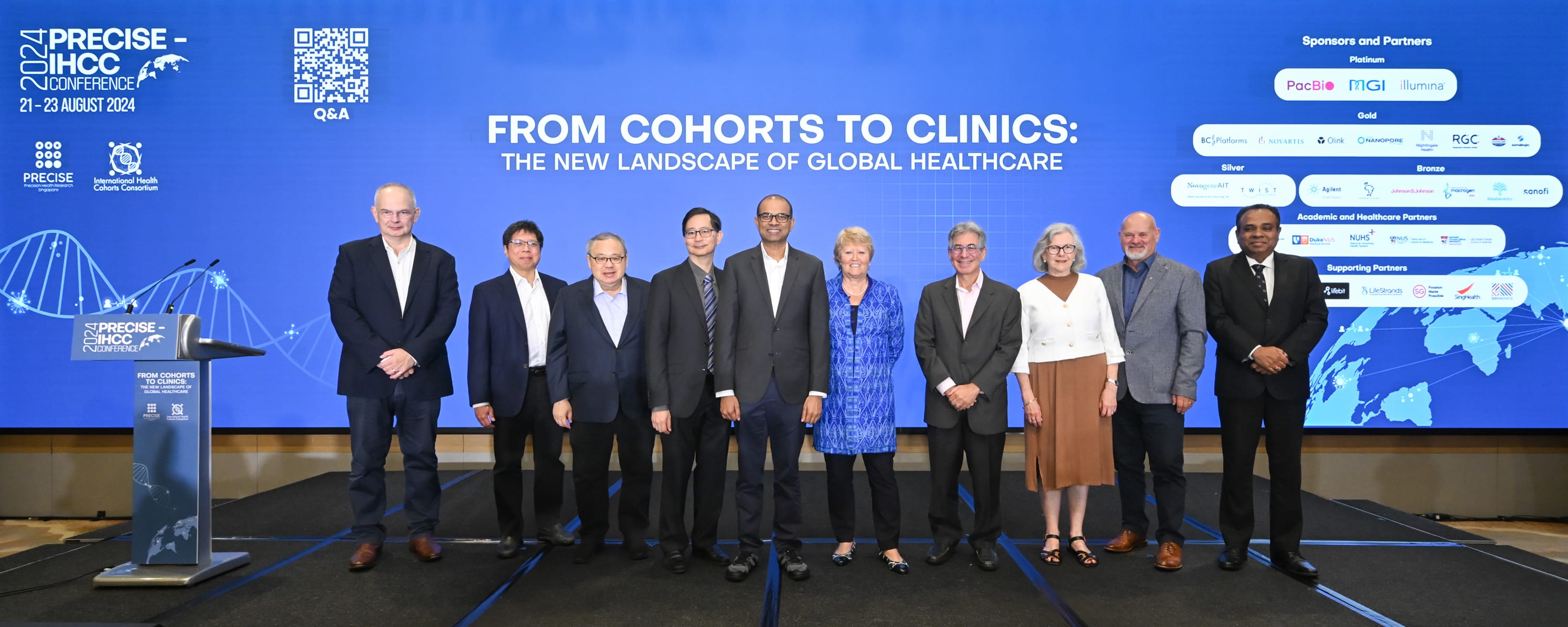 Eight people stand in front of a large blue screen displaying healthcare conference details and sponsor logos.
