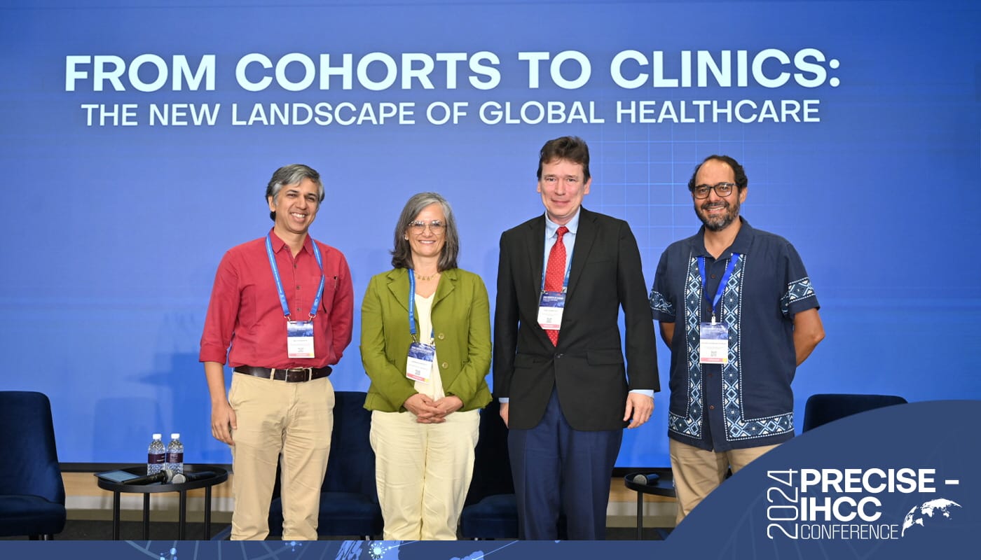Four people stand in front of a blue backdrop with text "From Cohorts to Clinics: The New Landscape of Global Healthcare."