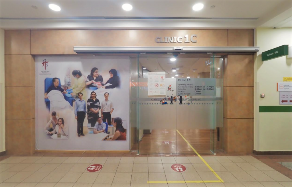 Entrance of Clinic 1C with a glass door, opening hours listed, and a wall poster showing medical personnel.