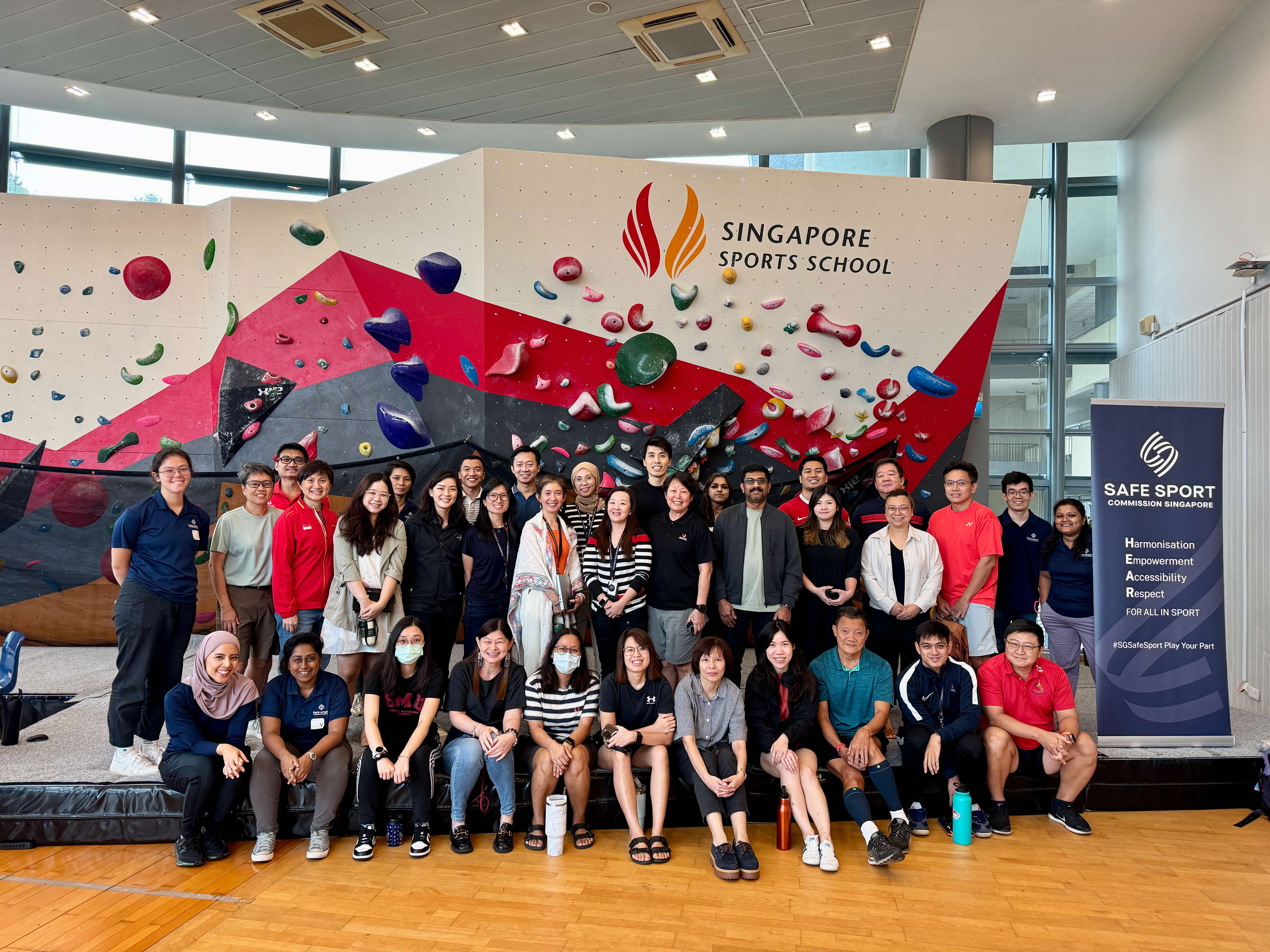A group of people standing and sitting in front of a colorful indoor climbing wall at Singapore Sports School.