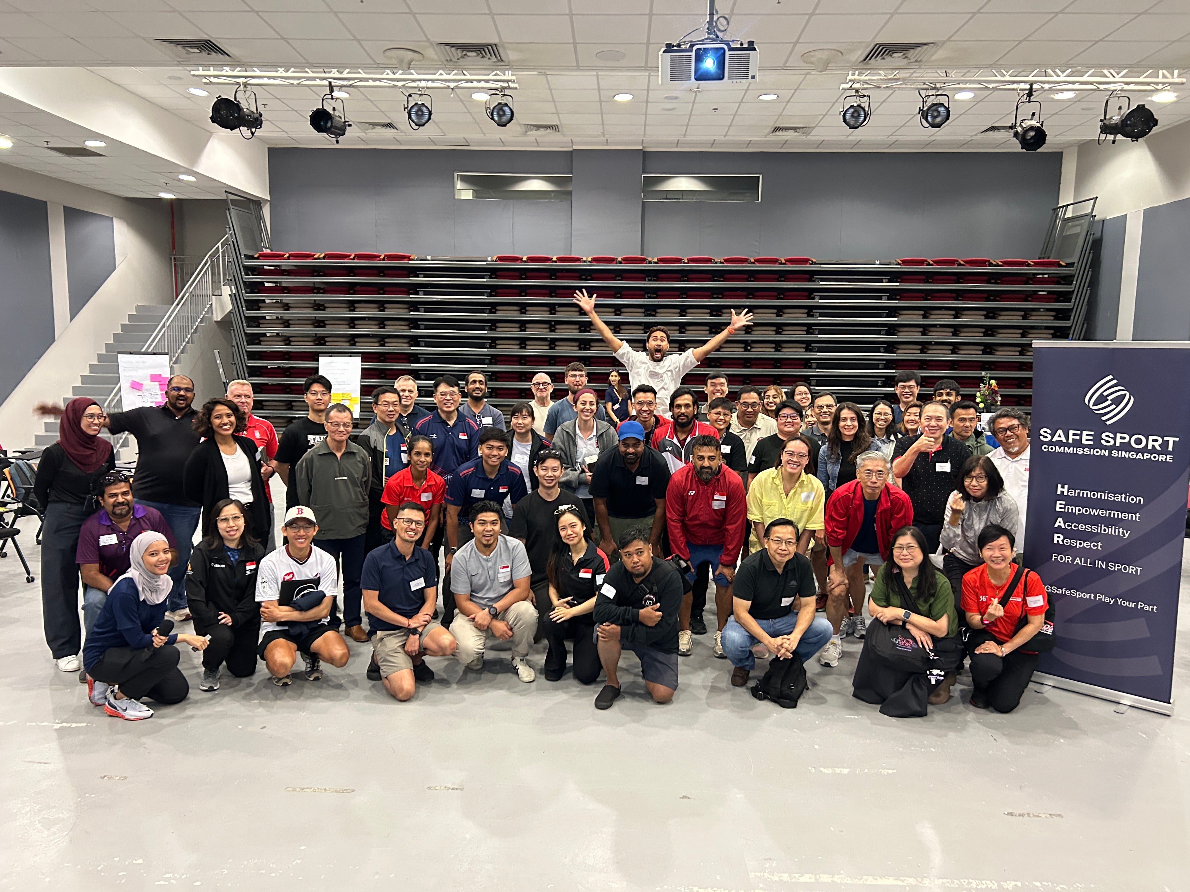 A diverse group of people smiling and posing together in a large auditorium setting.