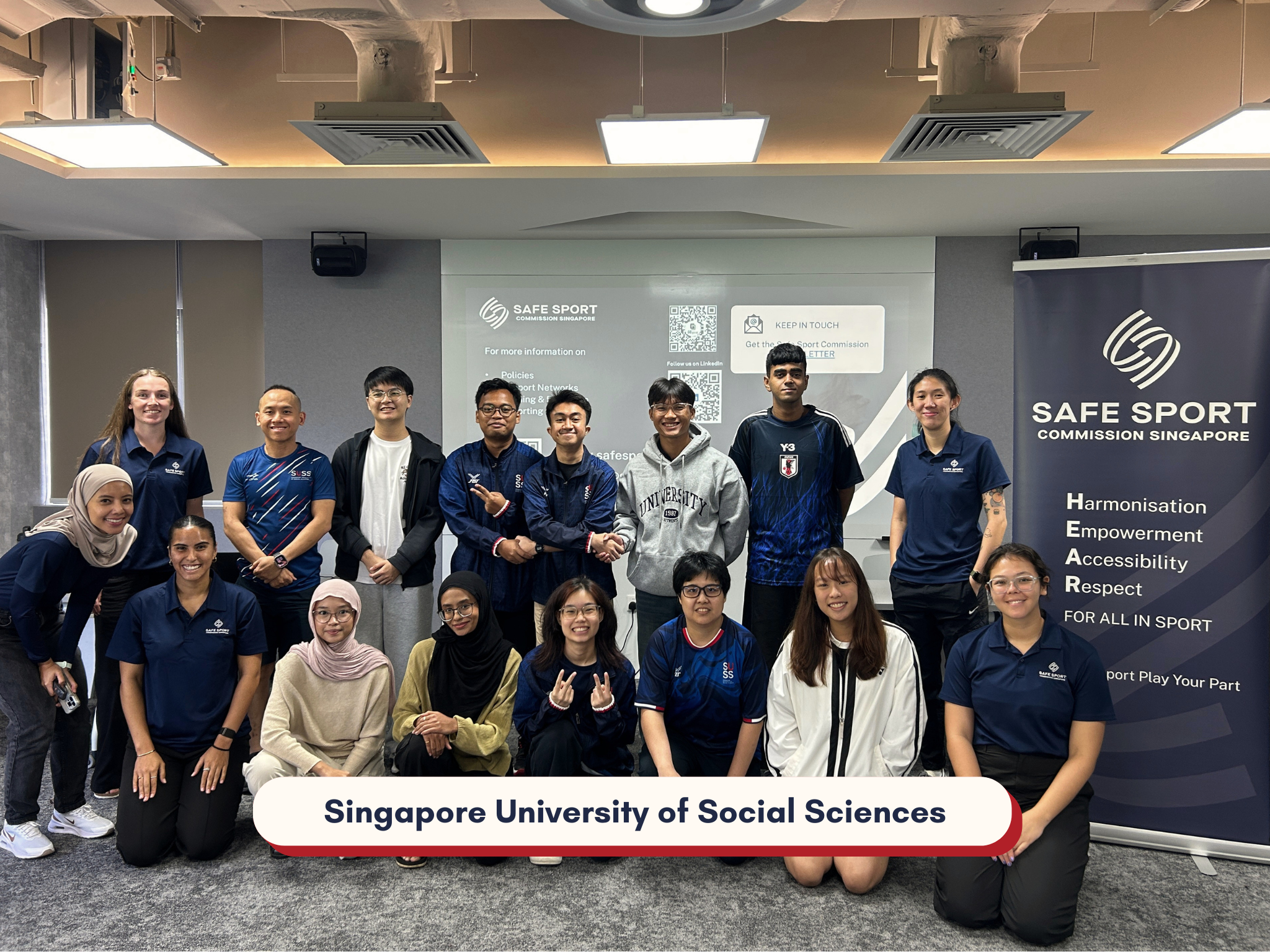 Group of diverse students and instructors at Singapore University of Social Sciences, standing indoors with a Safe Sport banner, smiling.