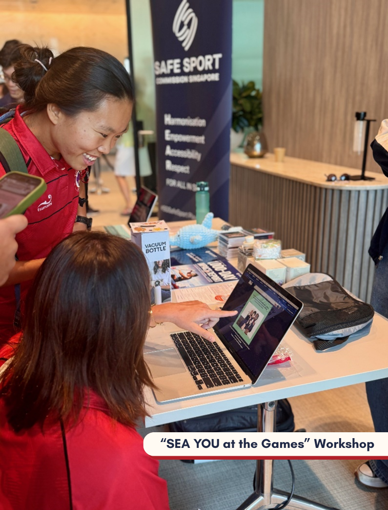 Two people wearing red play the Upstander Test on laptop on a table displaying workshop materials and a banner reads "Safe Sport Commission Singapore".