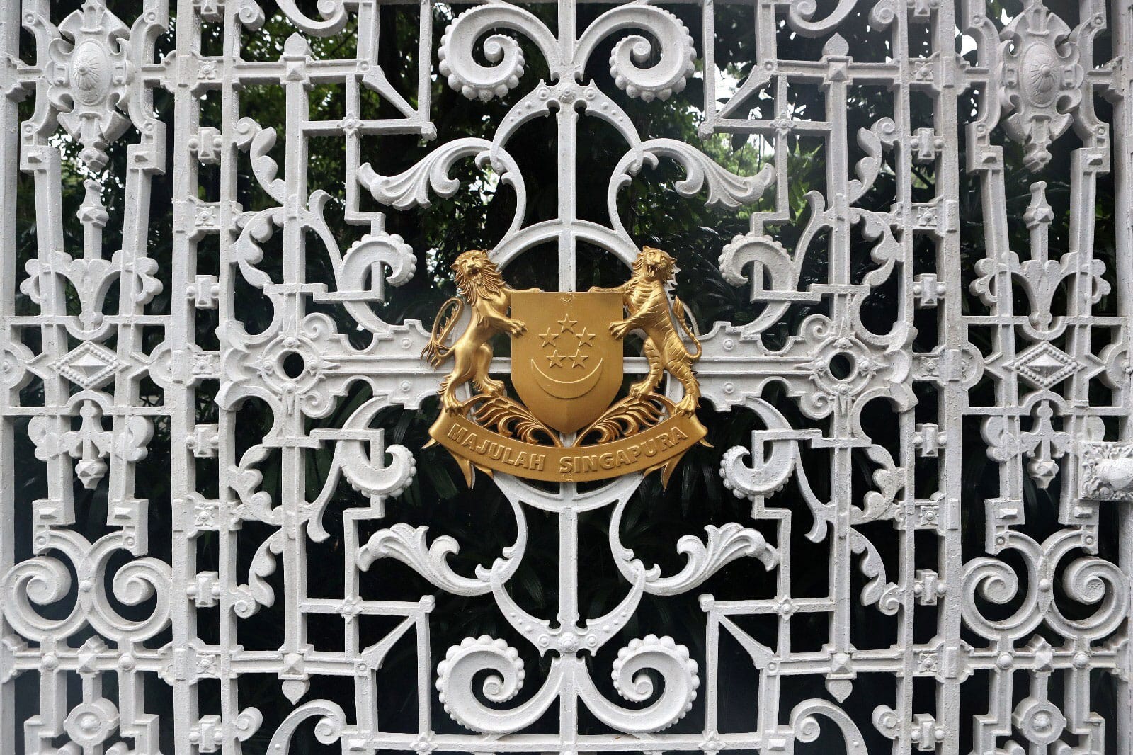 Ornate white metal gate with the gold Singapore coat of arms at center.