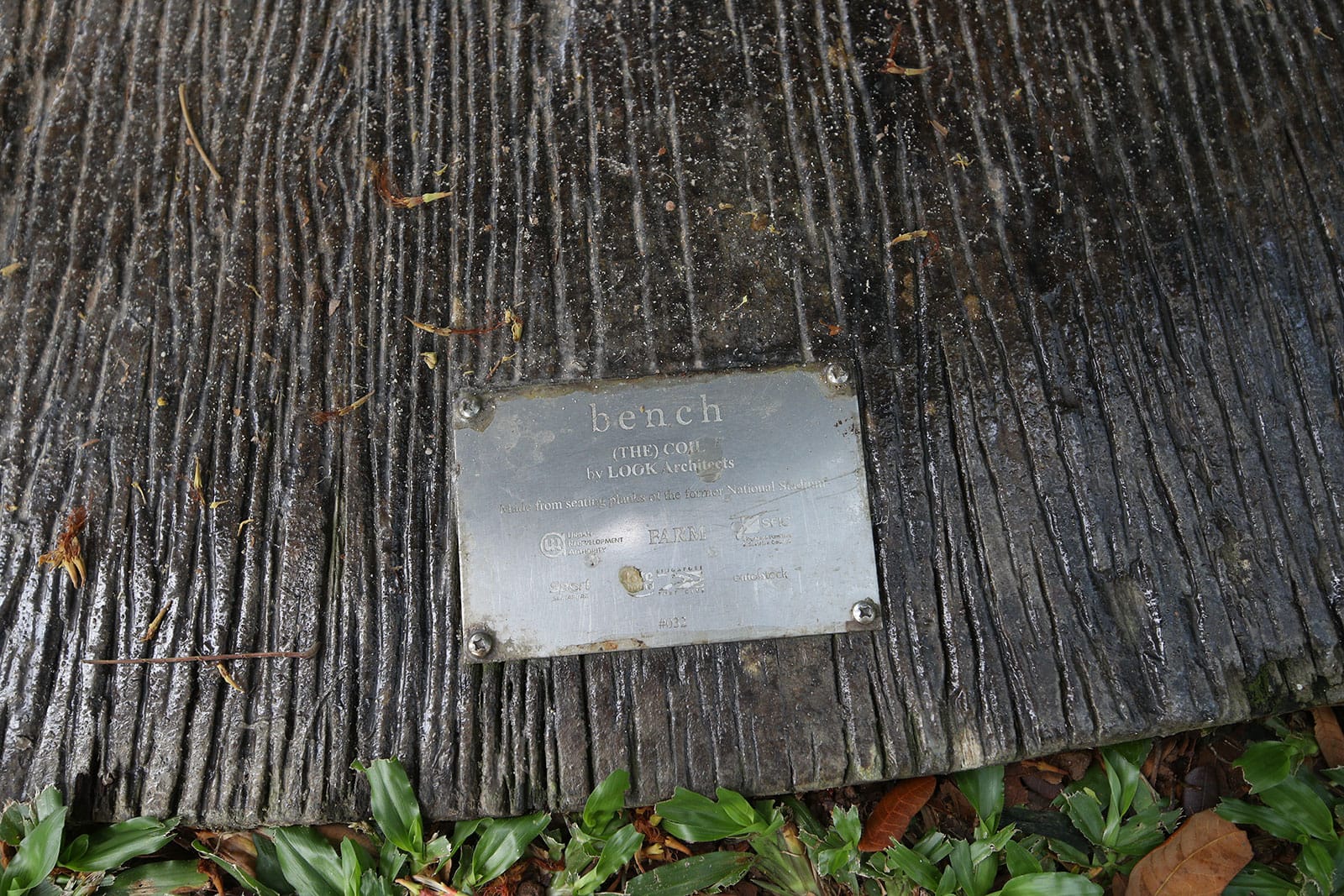 Textured bench surface with a metal plaque reading "bench (THE) COIL by LOOK Architects."