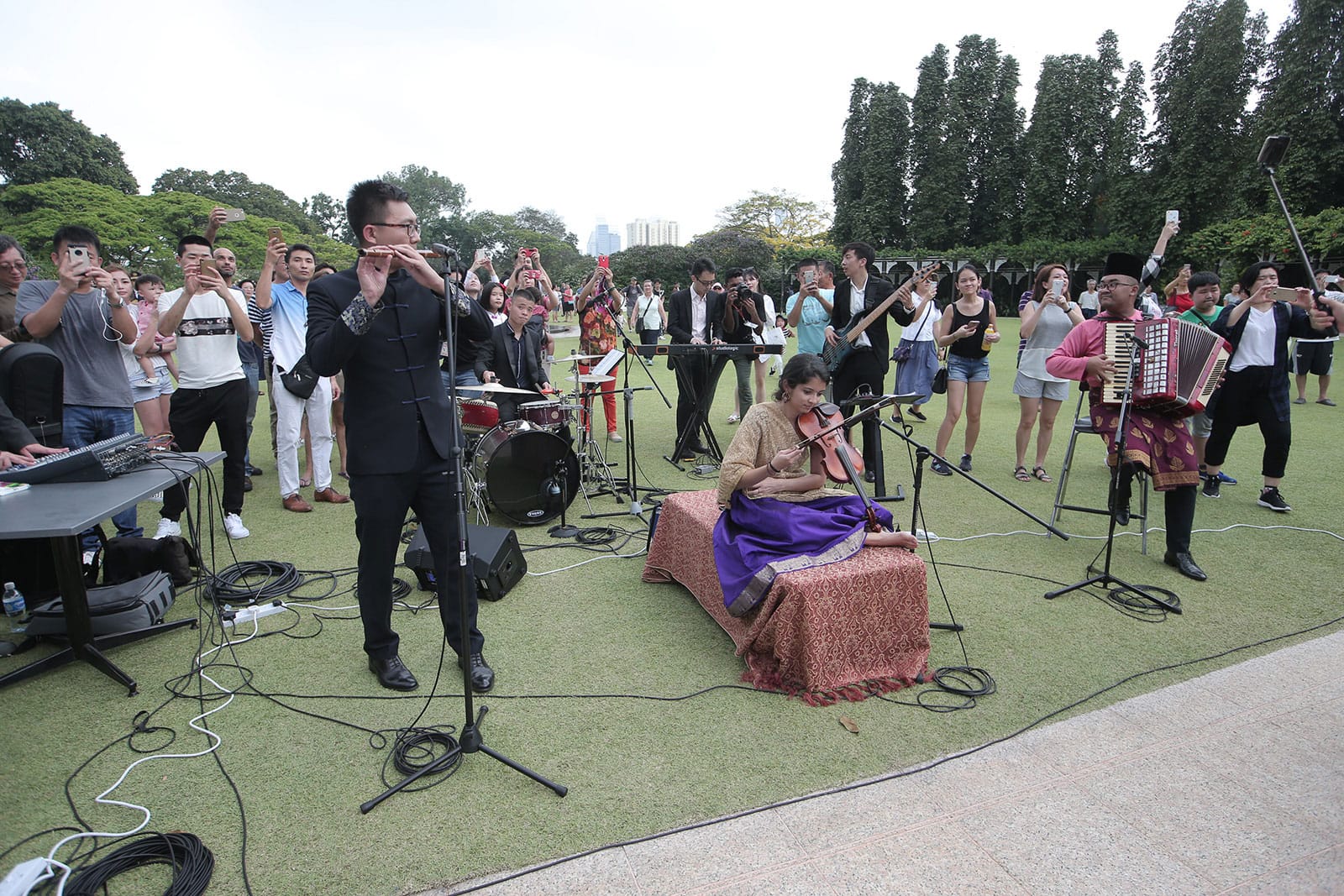 Outdoor musical performance; a band on green lawn playing for a crowd taking photos.