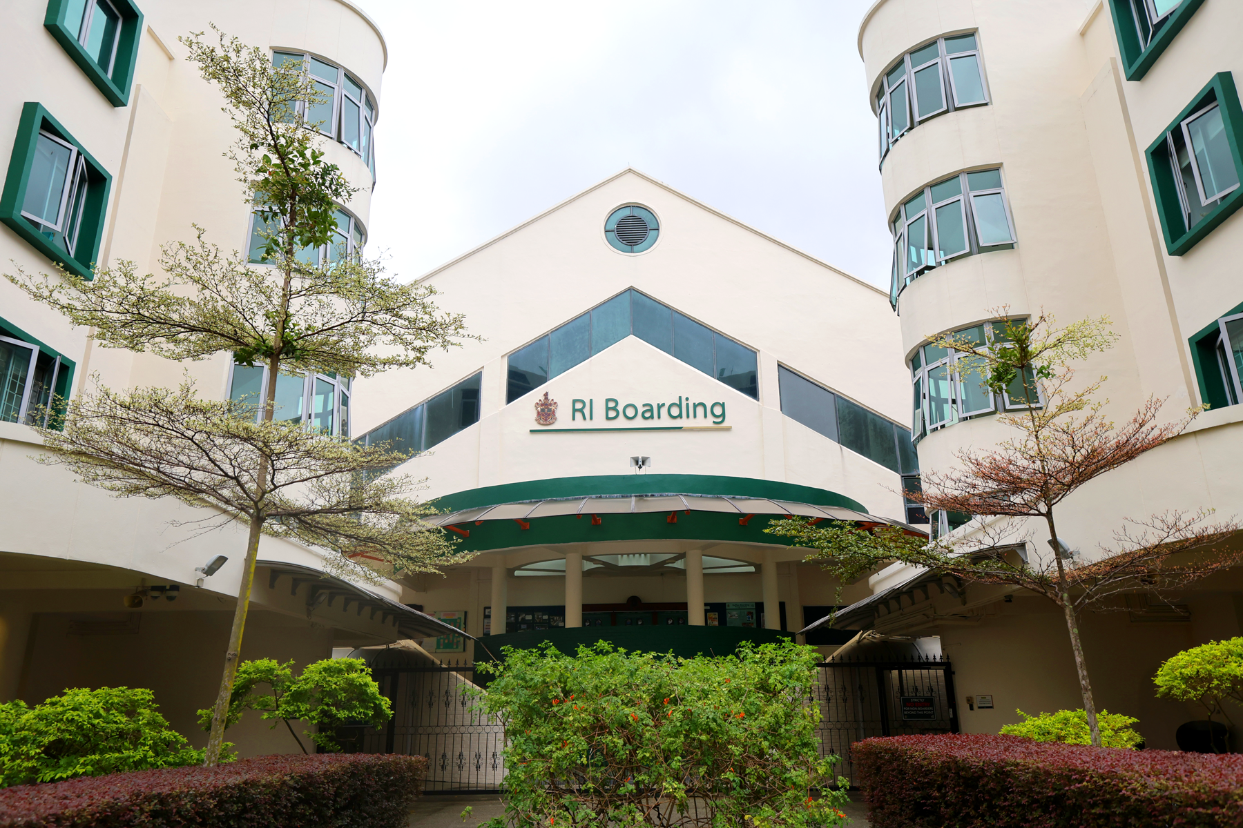 White multi-story building with green trim and a sign reading RI Boarding, flanked by trees and shrubs.