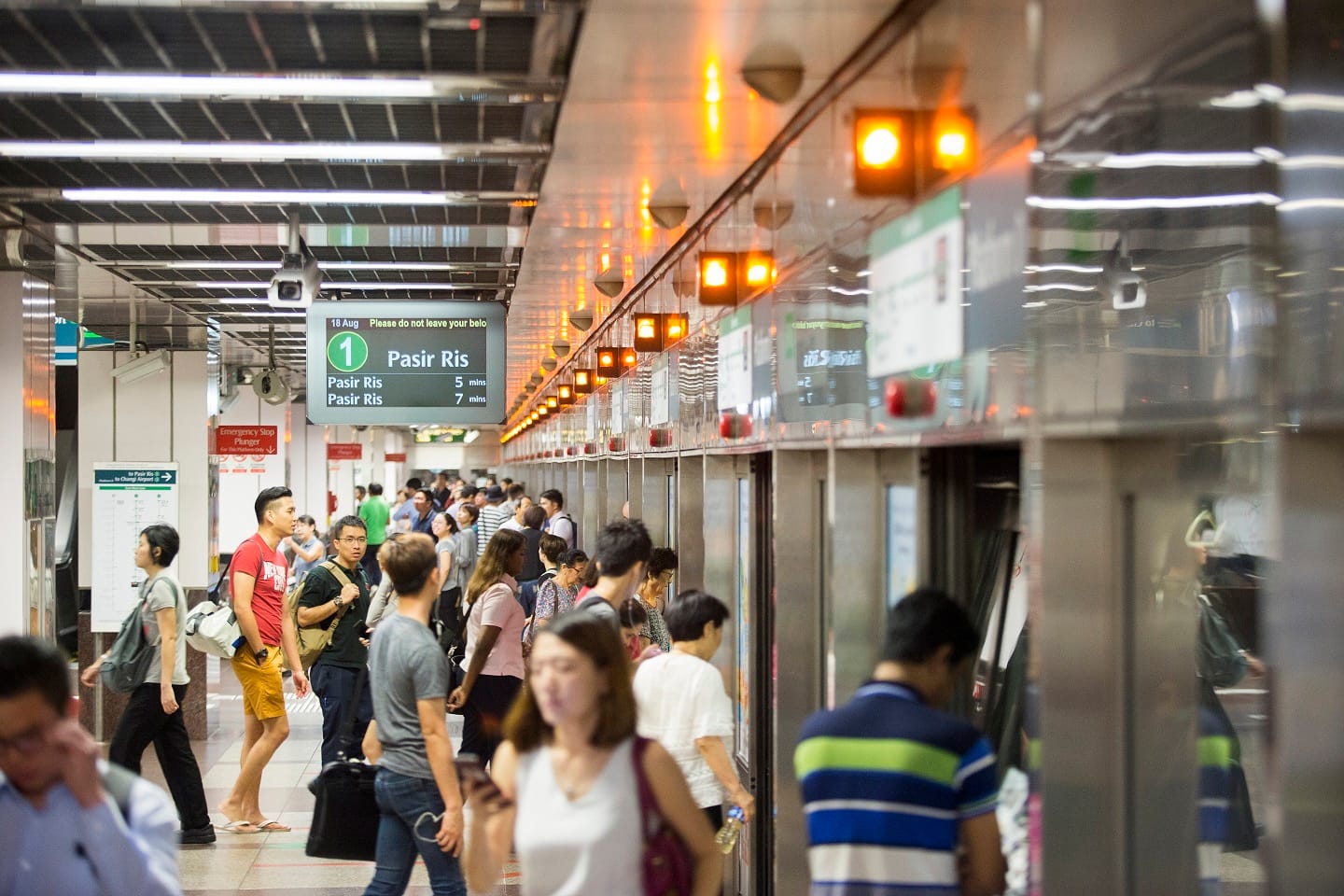Crowd of commuters waiting on an MRT platform with a display showing train arrivals to Pasir Ris in five and seven minutes.