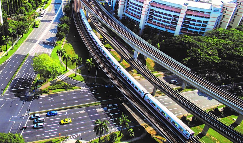 Aerial view of MRT trains traveling on parallel elevated tracks through an urban area.