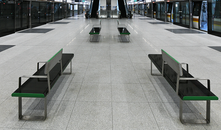 Empty MRT platform with green-trimmed benches and escalators in the background.