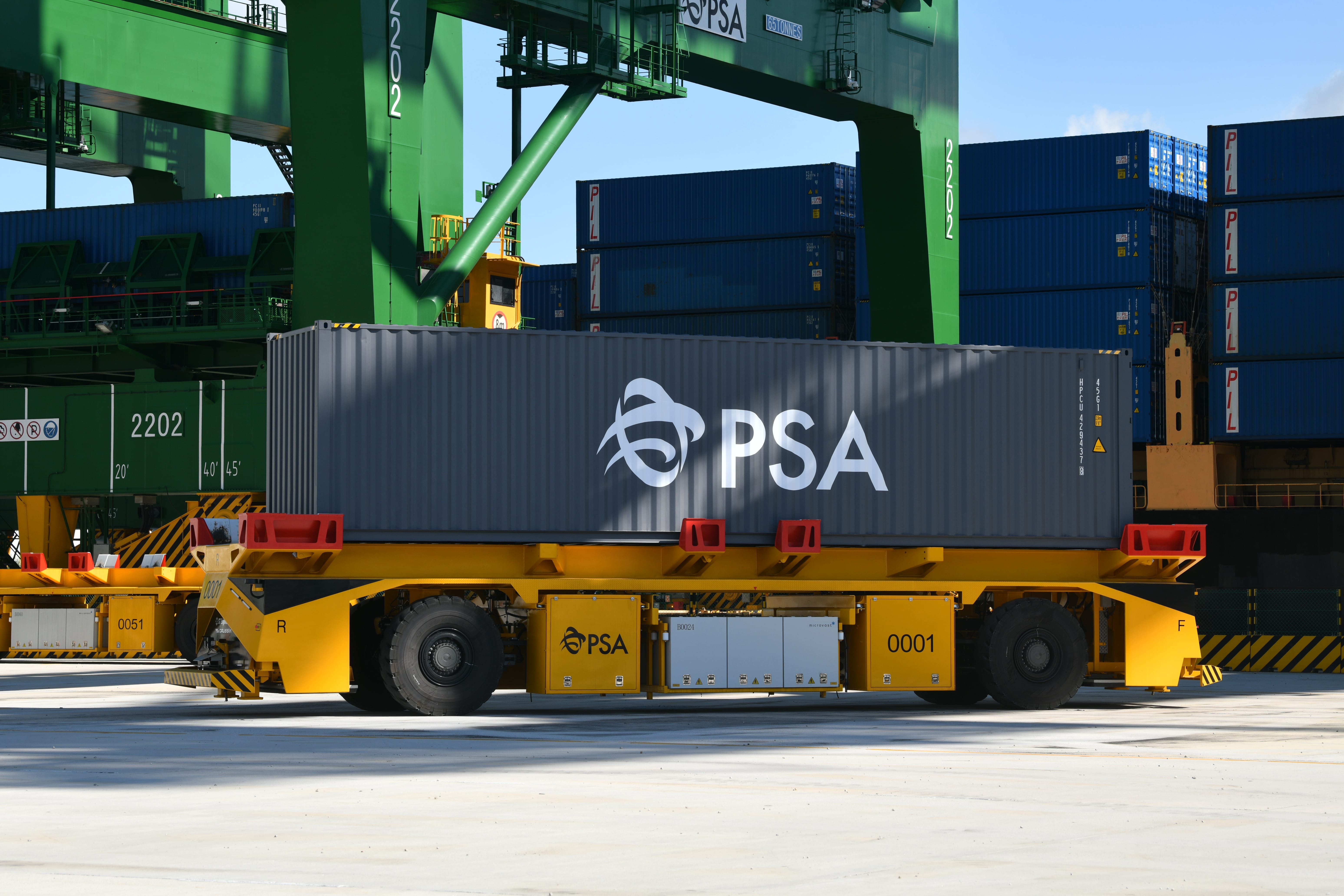 Yellow automated guided vehicle transporting a PSA-branded cargo container at a port terminal.