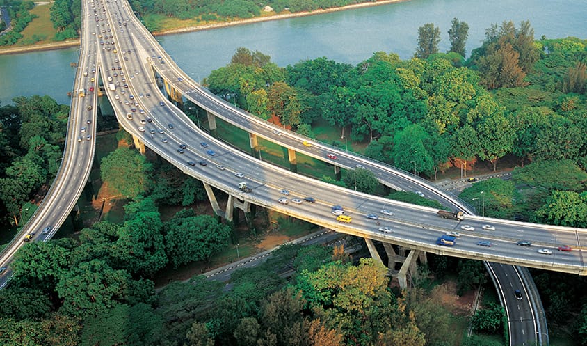 Aerial view of Benjamin Sheares Bridge with vehicles driving over elevated expressways surrounded by greenery and water.