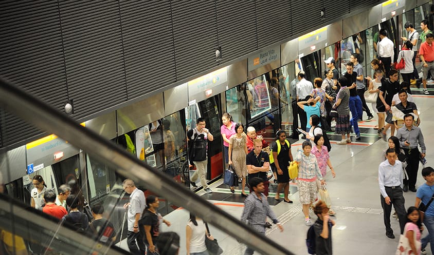 Commuters waiting and boarding trains at a busy MRT platform with glass safety doors.