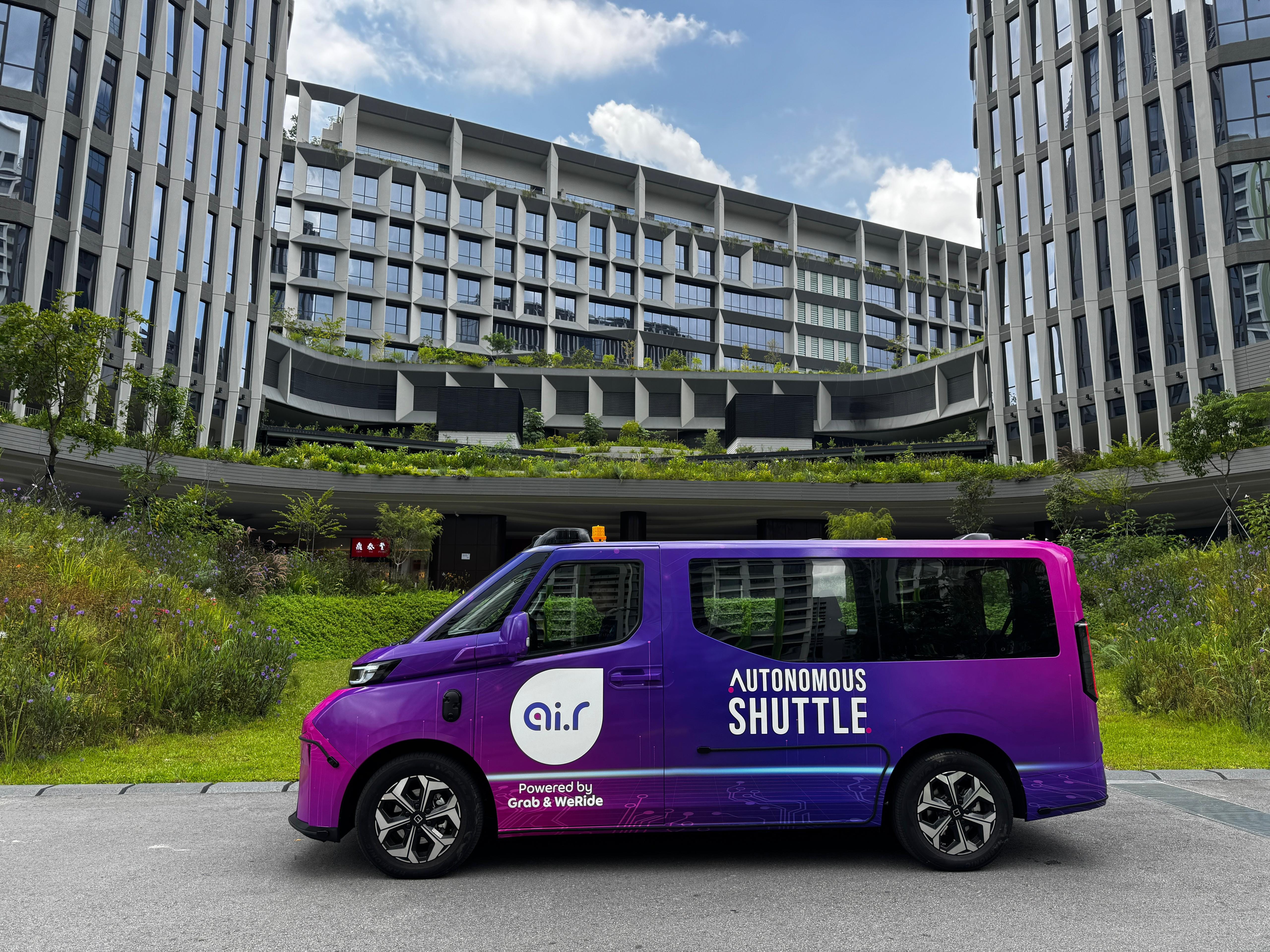 Purple autonomous shuttle displayed outdoors amid modern buildings with greenery.
