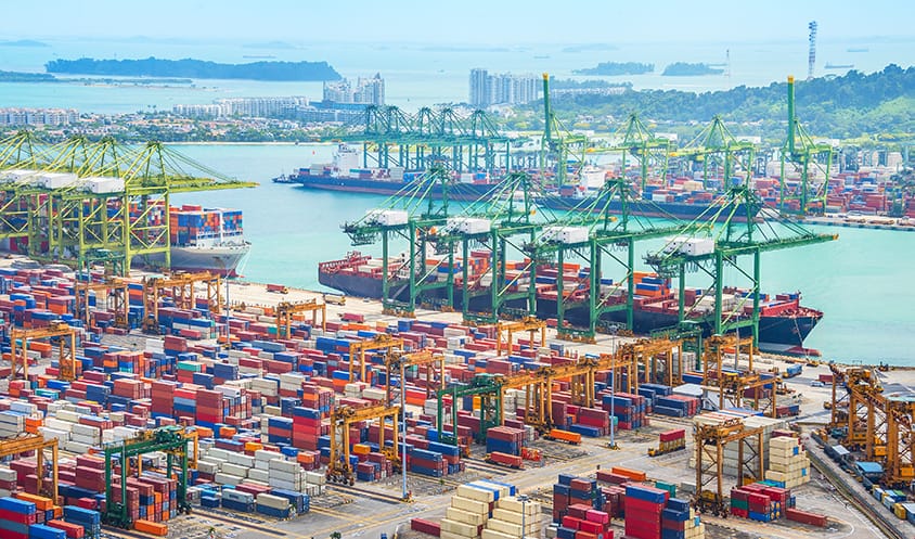 View of a busy container port with colorful stacked containers, cranes, and ships docked along the waterfront.