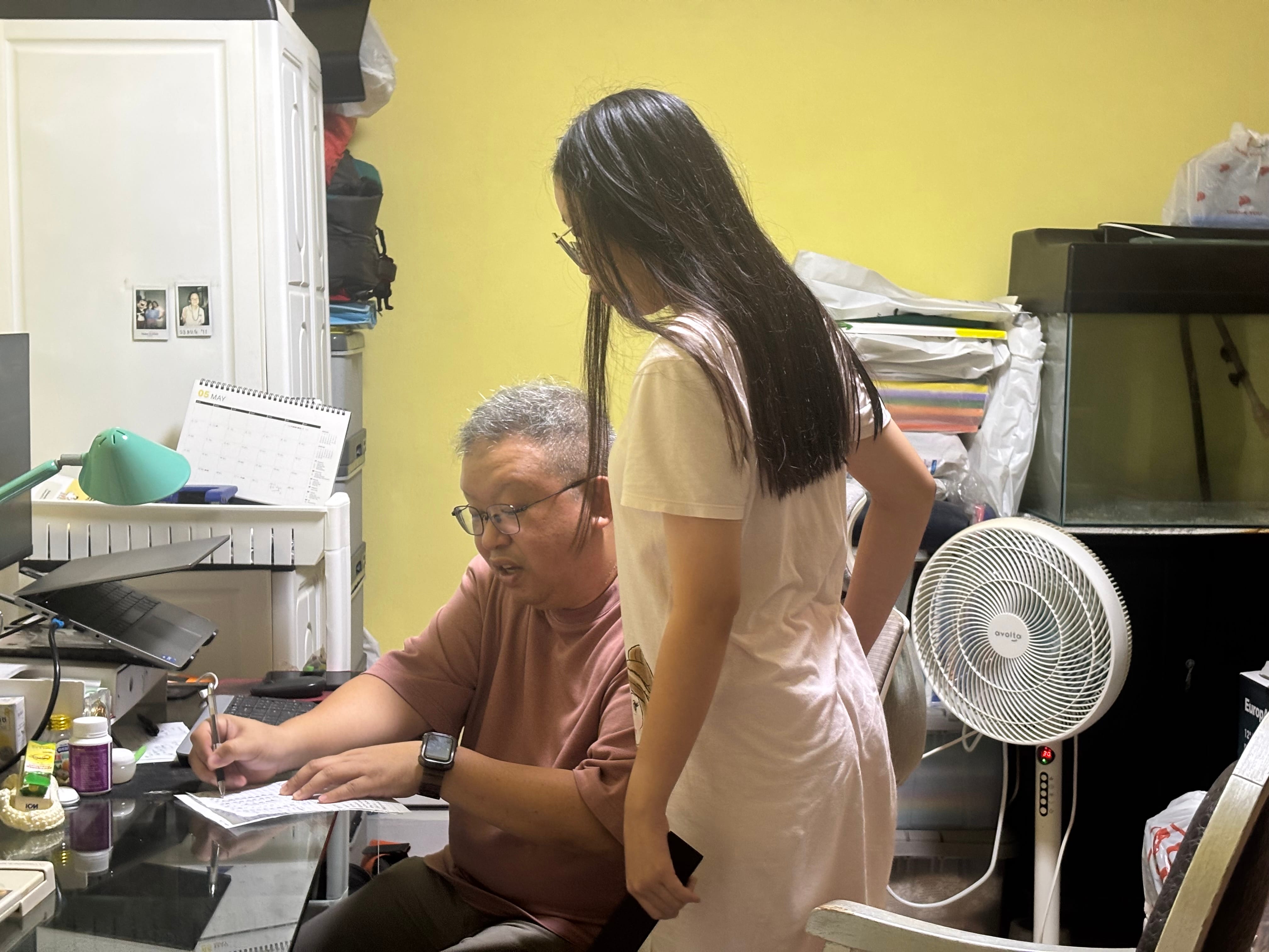 Father sitting down helping his daughter with her homework while she stands
