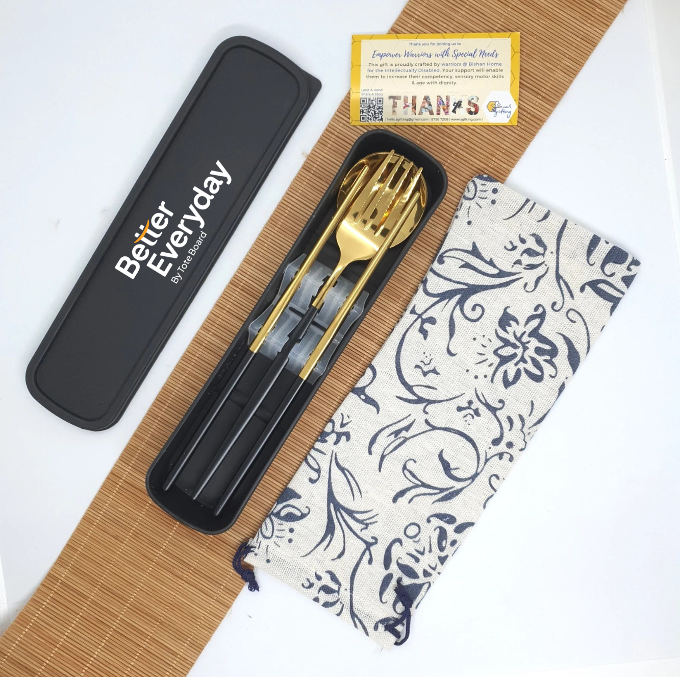 Gold cutlery set with black handles, pouch, and “Better Everyday” case on a bamboo mat.