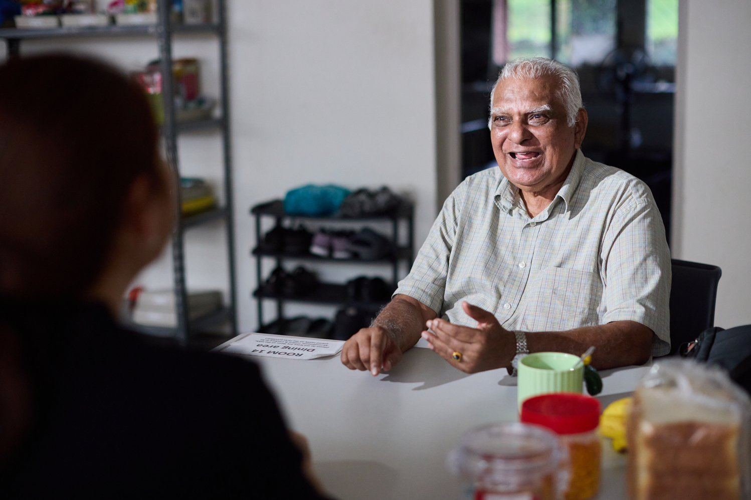 An elderly gentleman smiles warmly as he converses across a dining table