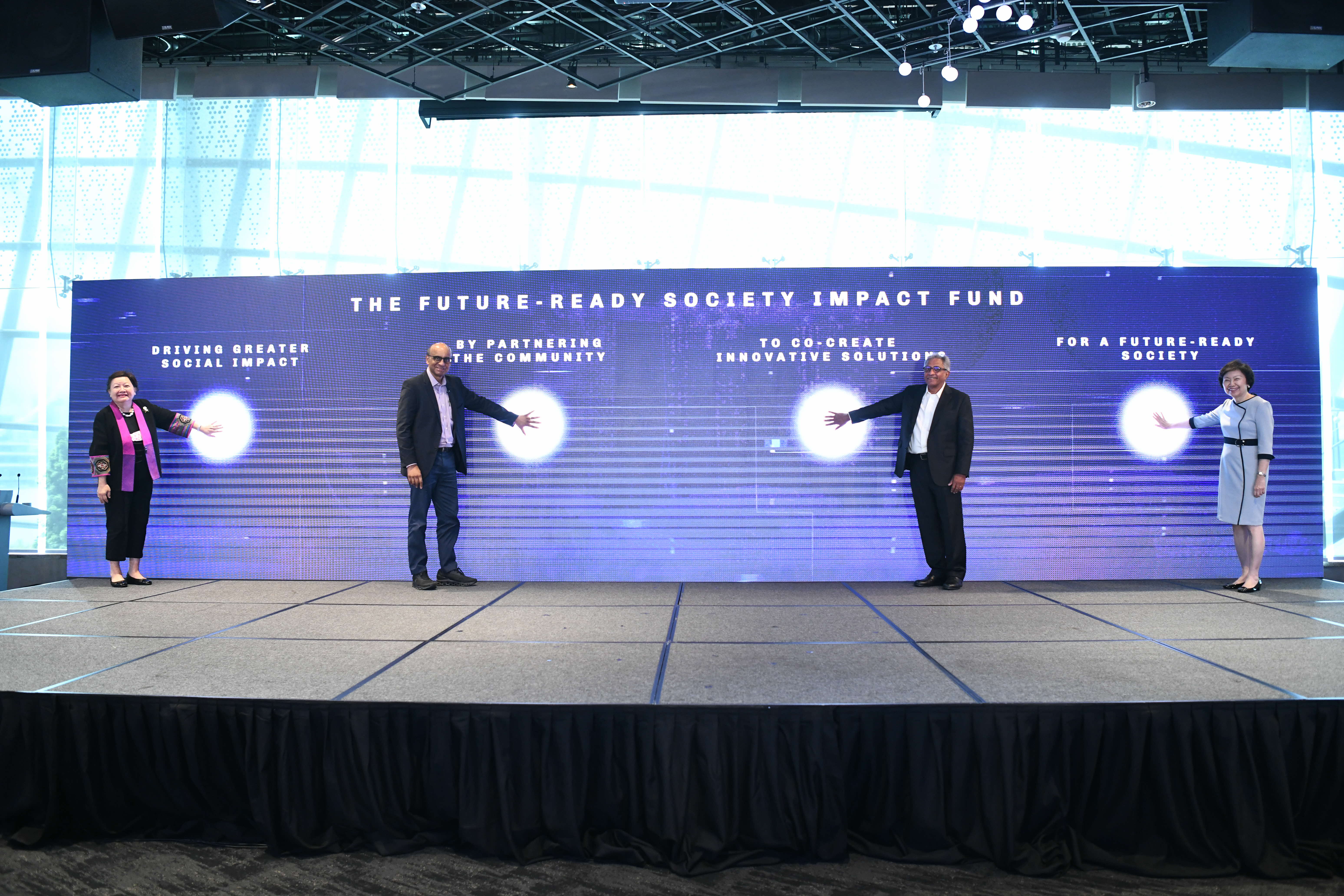 Four speakers on stage launching the Future-Ready Society Impact Fund, each touching a lighted display.
