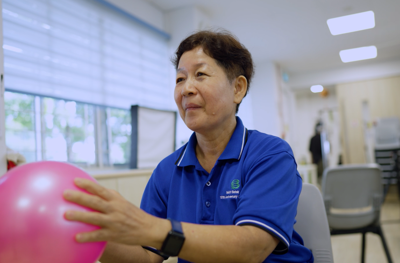 A lady in blue polo t-shirt exercising with a pink ball.