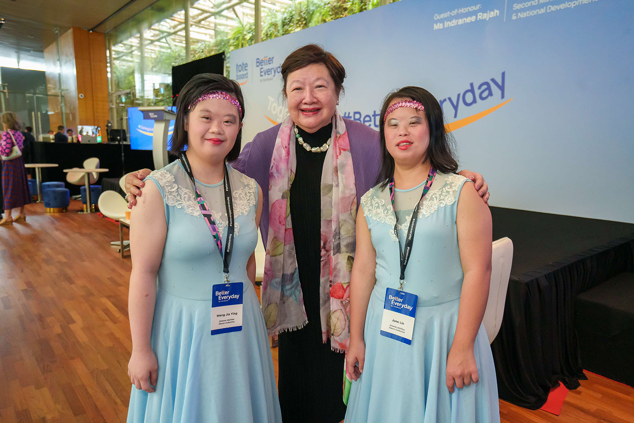 Chairman Mildred Tan with two dancers in blue performance outfits.