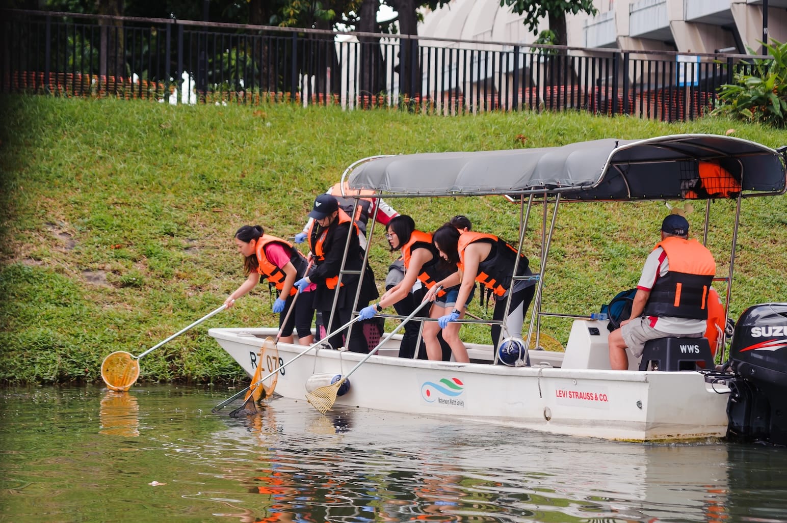 People in life vests on a Levi Strauss & Co. boat, using nets to collect debris from water.