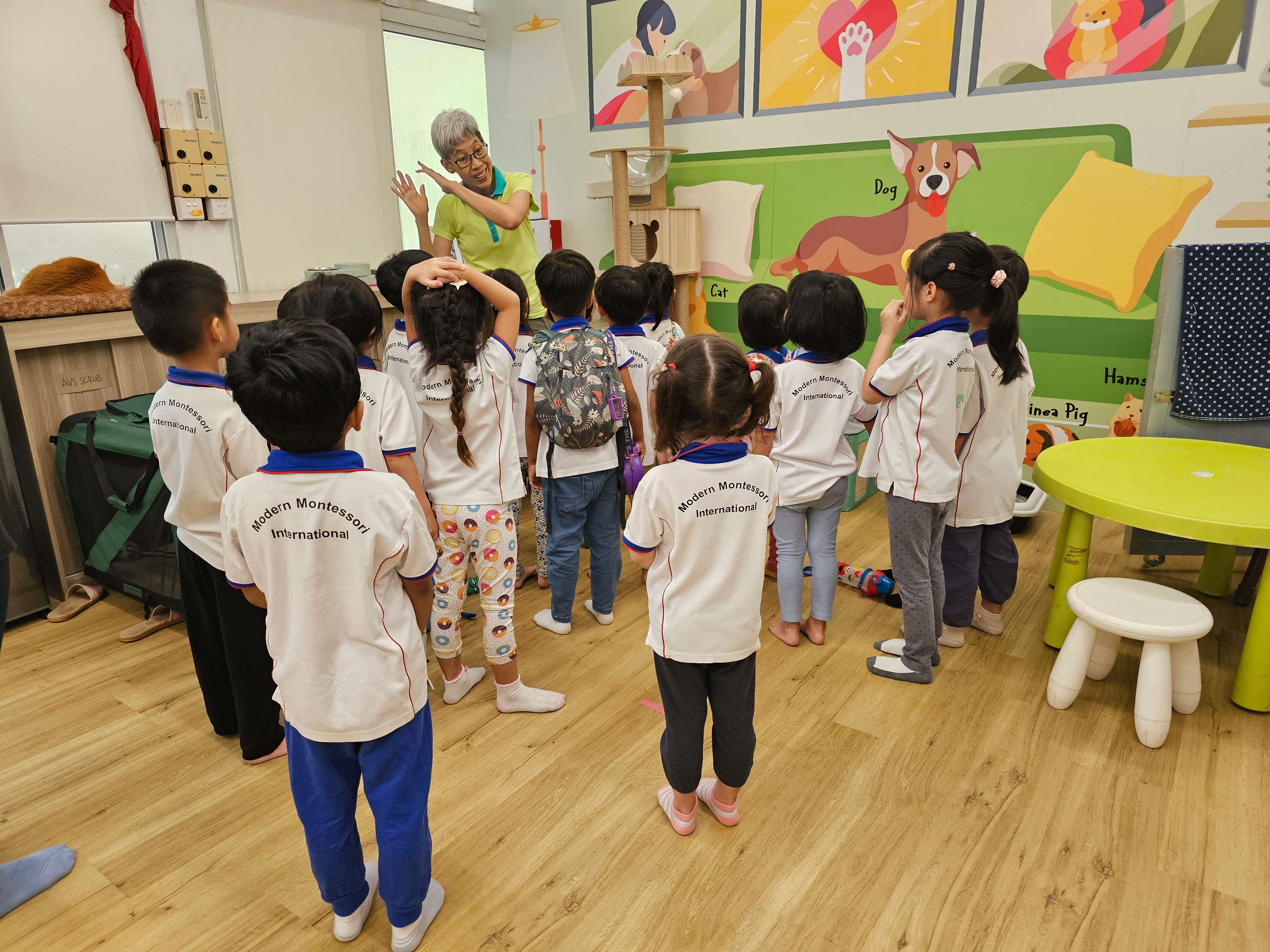 A photograph of a group of children listening to a presenter in a pet-themed classroom