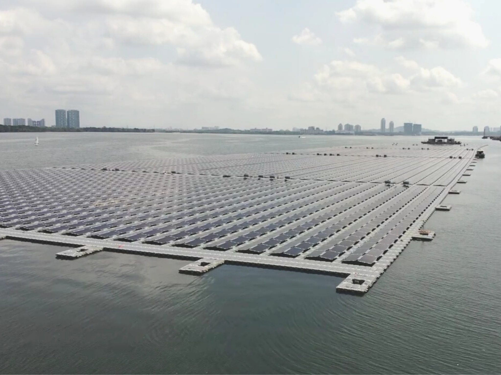 A large array of floating solar panels is installed on a body of water, with a city skyline visible in the background.