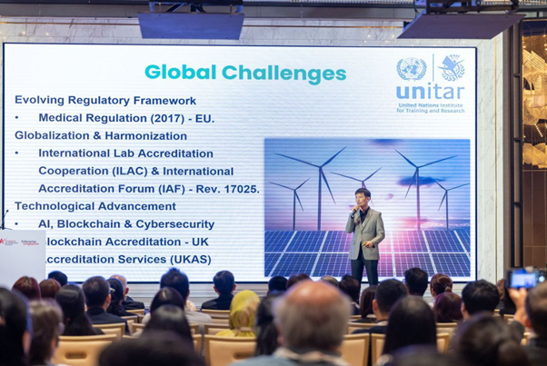 A speaker presents a UNITAR "Global Challenges" slide about regulation, AI, and blockchain to a seated audience.