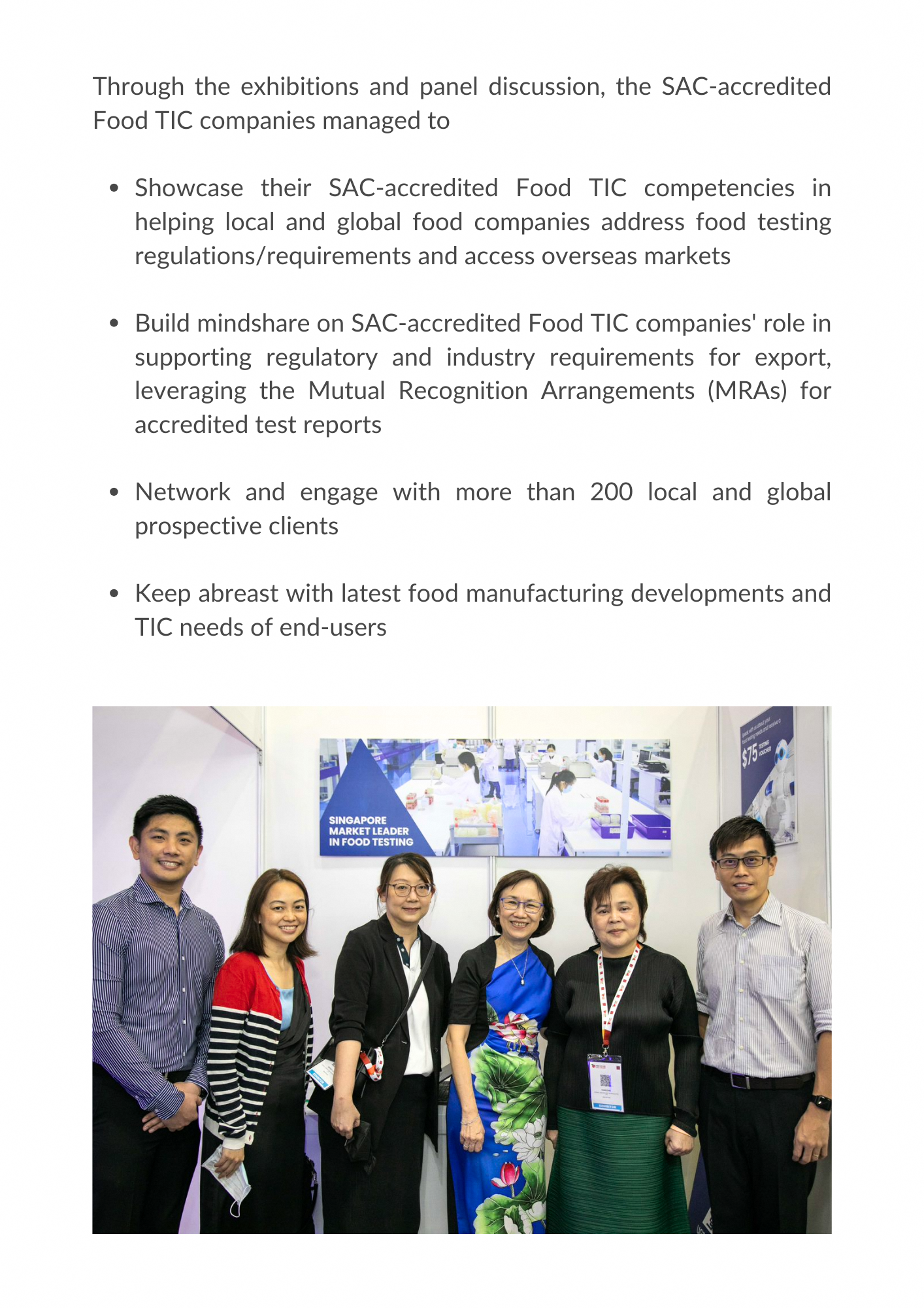Six people smiling and posing at a Singapore Market Leader in Food Testing exhibition booth.