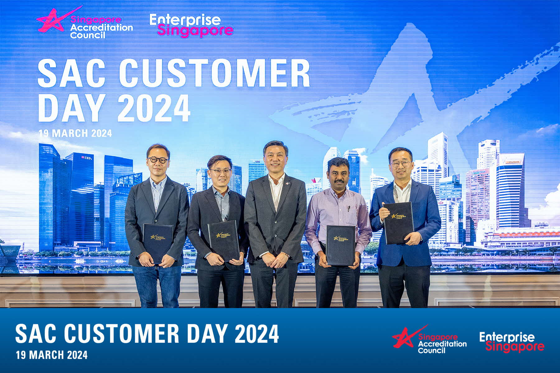 Five people stand holding folders in front of a SAC Customer Day 2024 banner dated 19 March 2024.