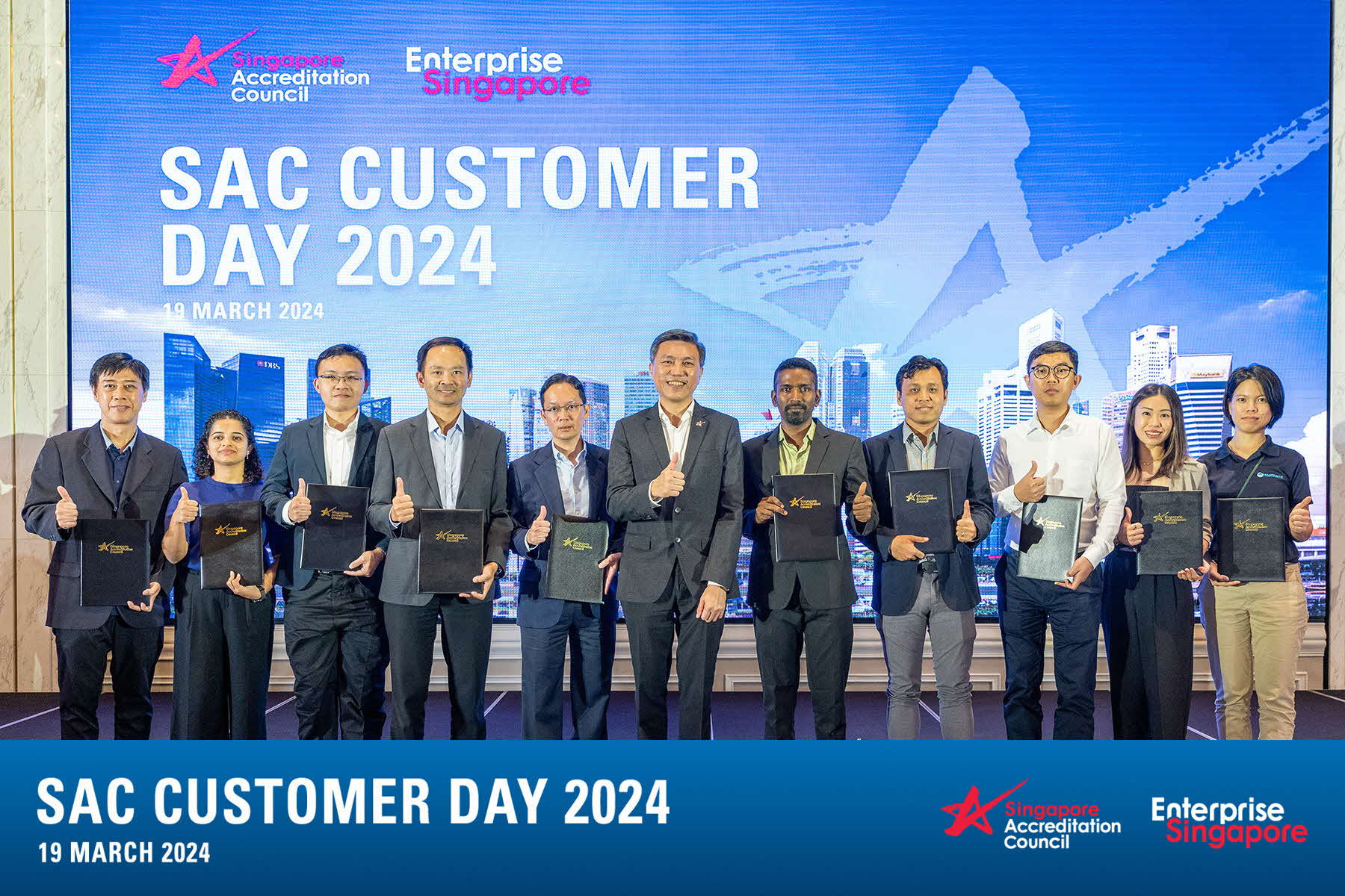 Group on stage holding certificates, giving thumbs up before SAC Customer Day 2024 backdrop dated 19 March 2024.