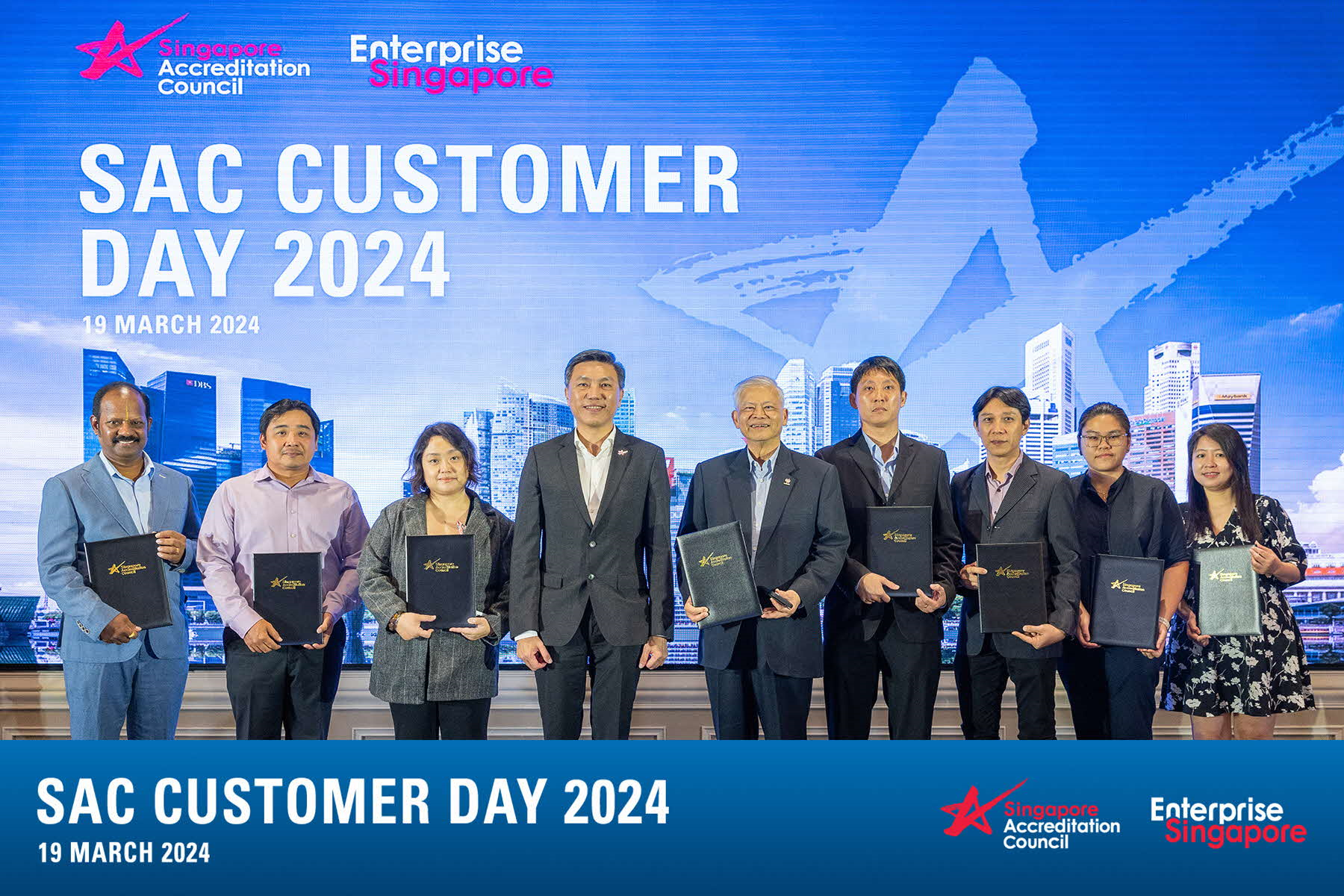 Nine people stand holding black folders at SAC Customer Day 2024 on 19 March 2024 in Singapore.