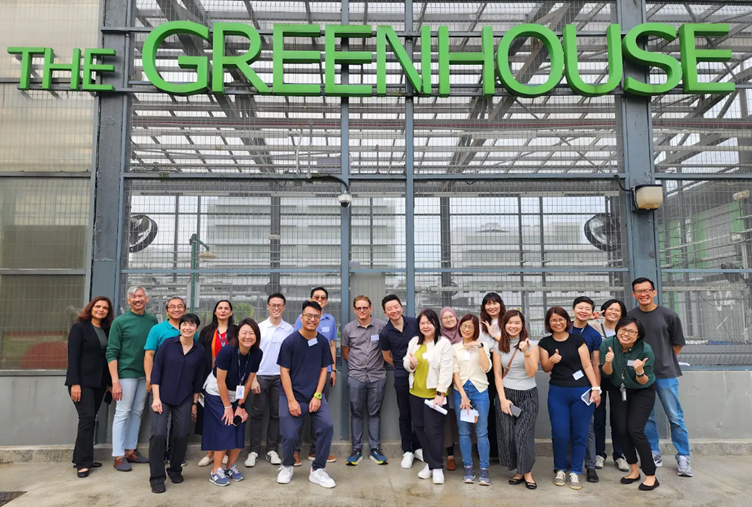 A group of people pose in front of a building with the sign "THE GREENHOUSE" in large green letters.