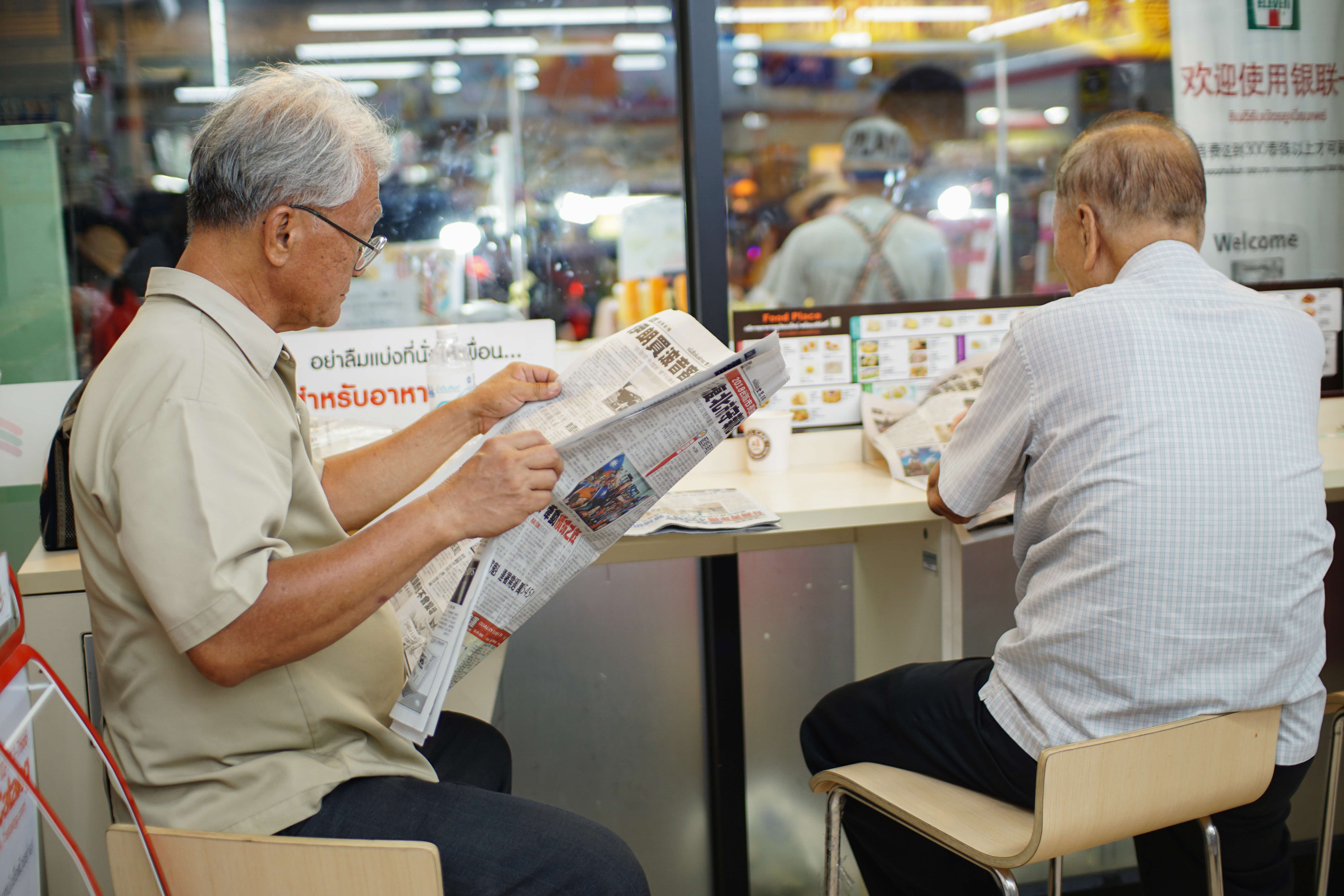 2 elderly men reading a Chinese newspaper